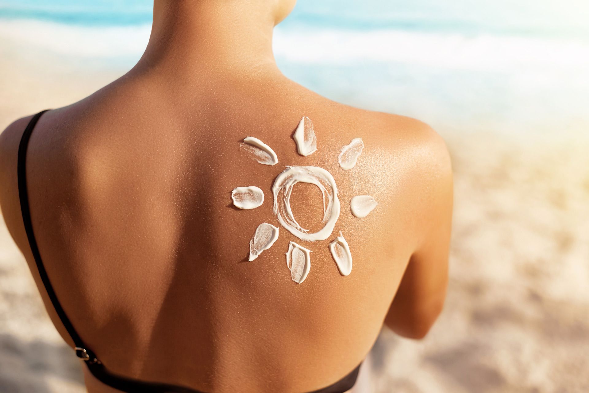 A woman is applying sunscreen to her back on the beach