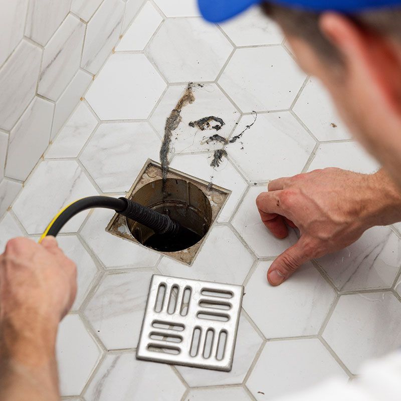 plumber unclogging blocked shower drain with hydro jetting at home bathroom. sewer cleaning service