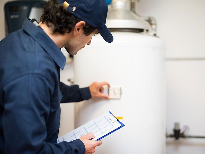 Man in blue uniform inspecting water heater with clipboard.