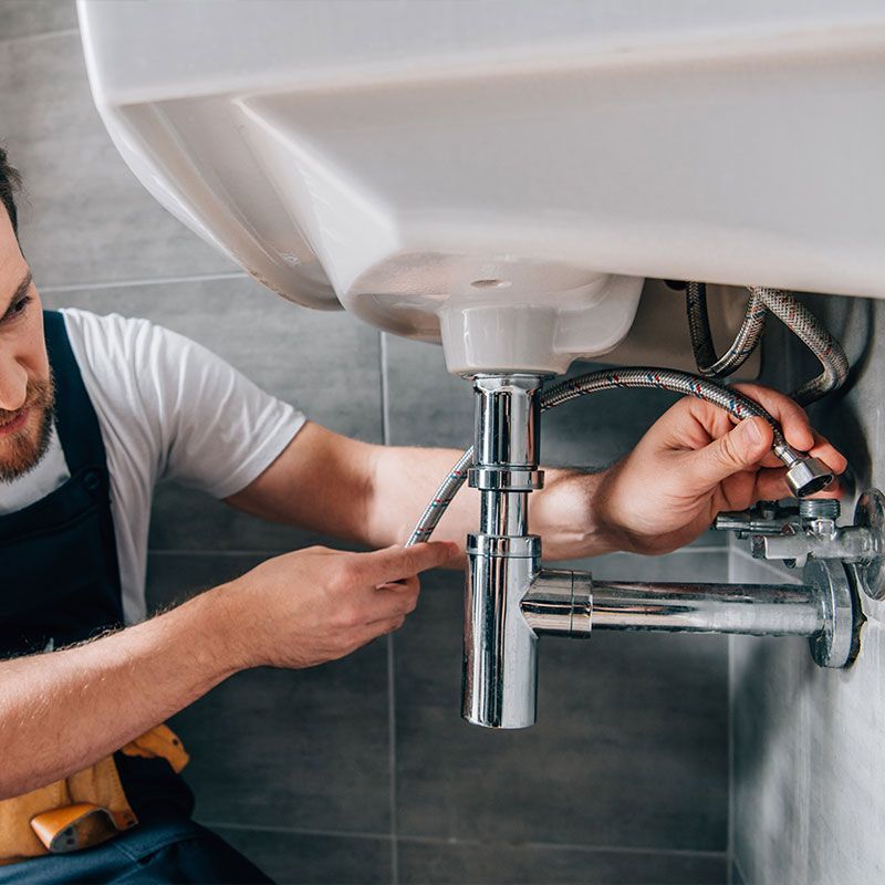 serious male plumber in working overall fixing sink in bathroom