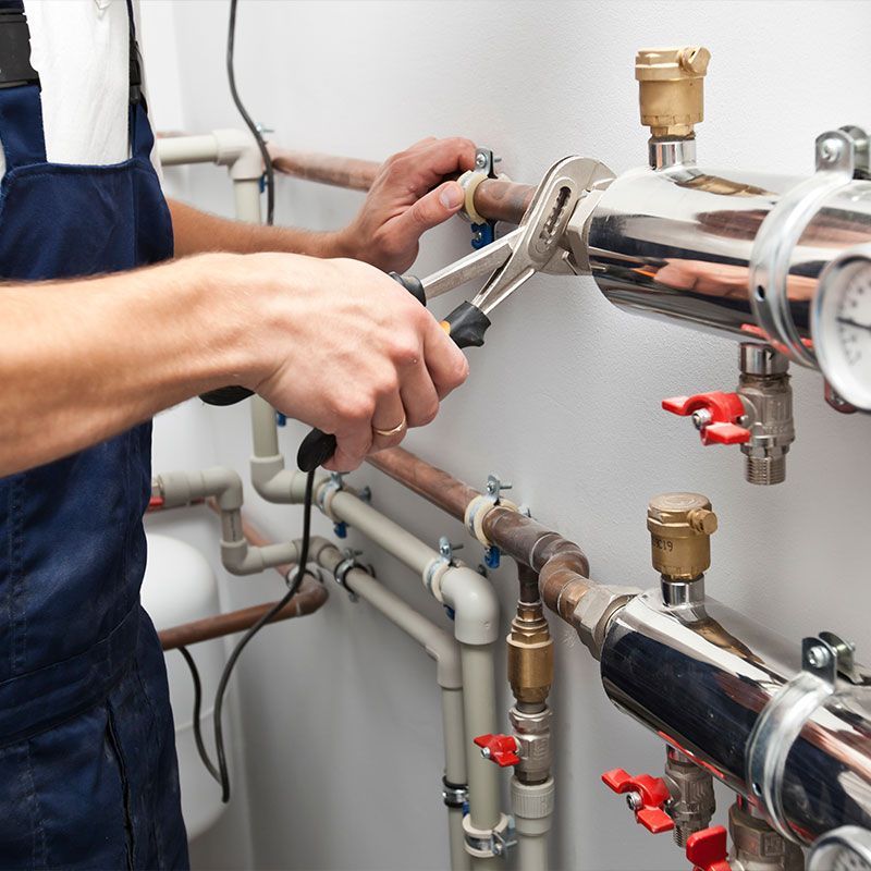 The man is installing the heater system in the house and checking pipes by the wrench