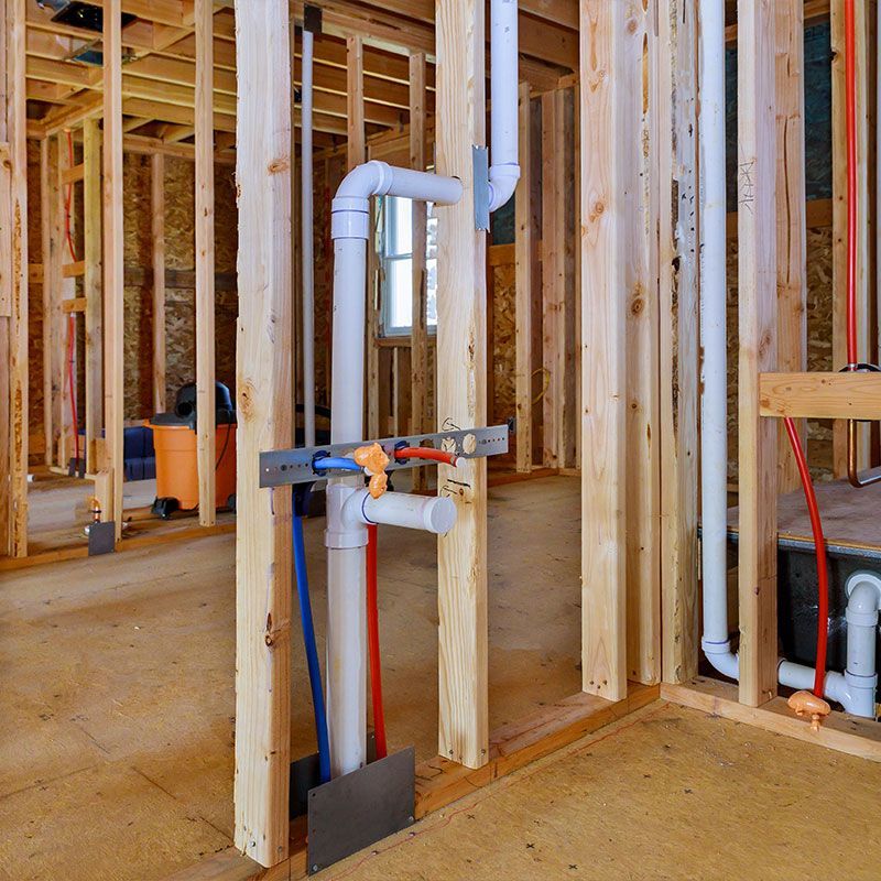 Applying pipe drain plumbing with hot red and cold blue pex pipe inside a house frame