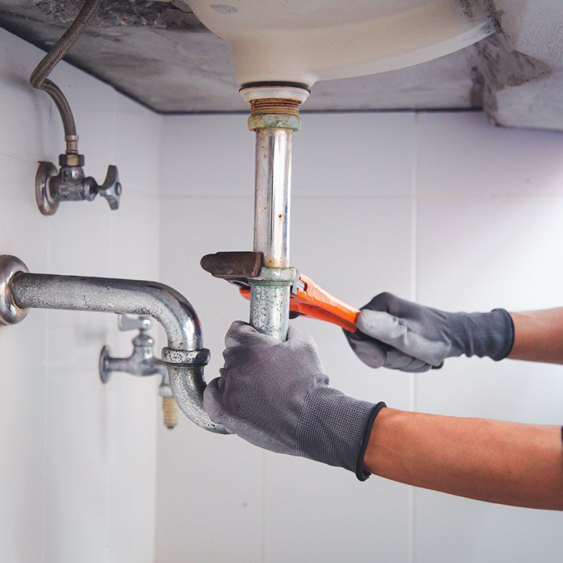 Technician plumber using a wrench to repair a water pipe under the sink. Concept of maintenance, fix water plumbing leaks, replace the kitchen sink drain, cleaning clogged pipes is dirty or rusty