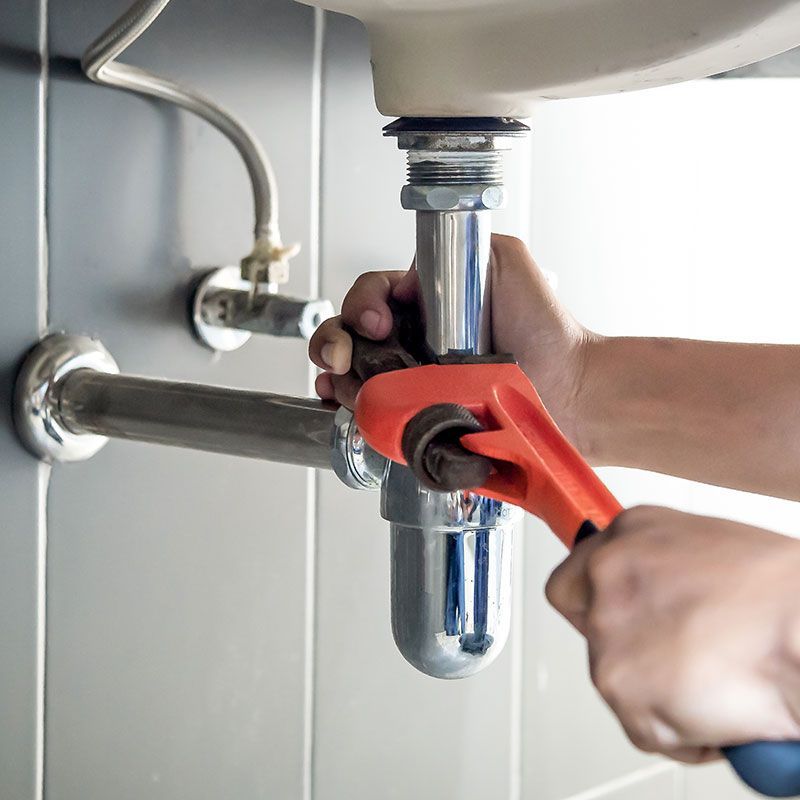 Plumber uses wrench to repair water pipe under sink There is maintenance to fix the water leak in the bathroom.with red wrench, plumbing install concept