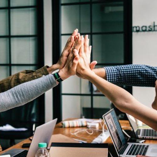La gente choca las manos sobre un escritorio con computadoras portátiles en un entorno de oficina.