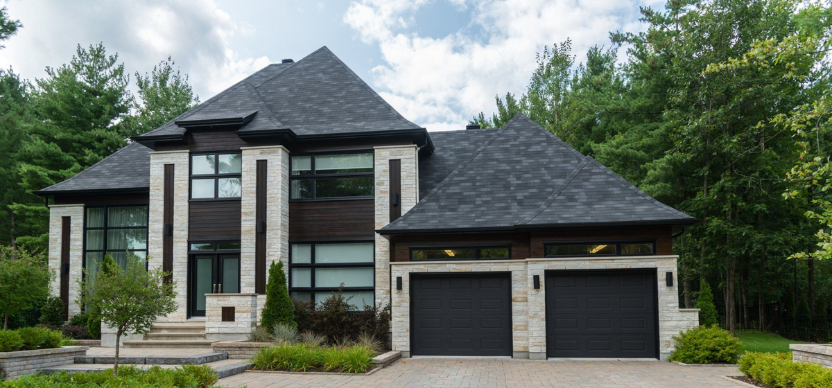 Modern two-story house with dark roof, two-car garage, and landscaped driveway