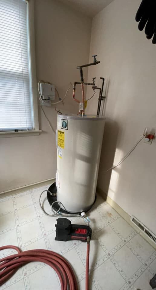 A water heater is sitting on the floor in a room next to a window.