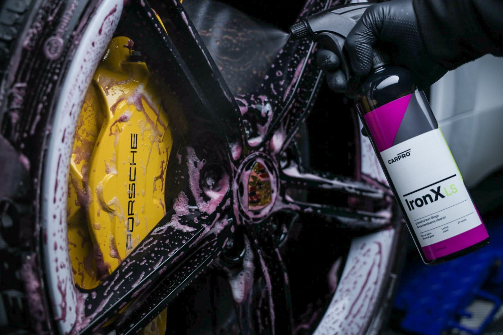 A person is cleaning a porsche wheel with a spray bottle.