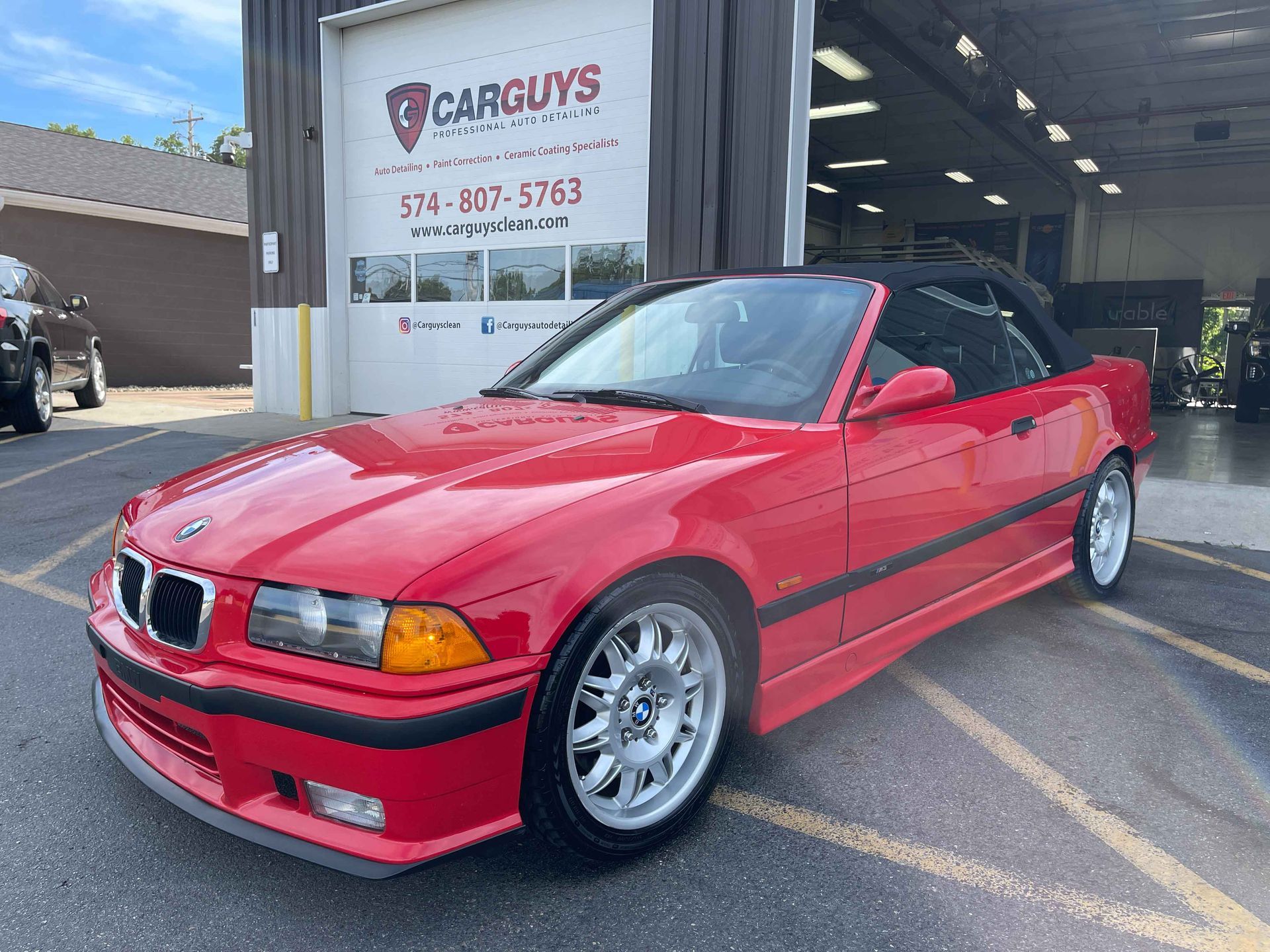 Red BMW E36 convertible parked in front of a car repair shop.