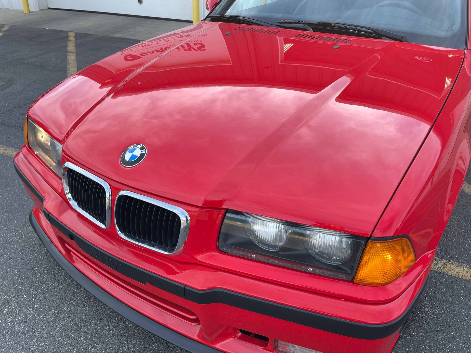 Red BMW car, front view. Hood with BMW logo, black grill, and headlights.