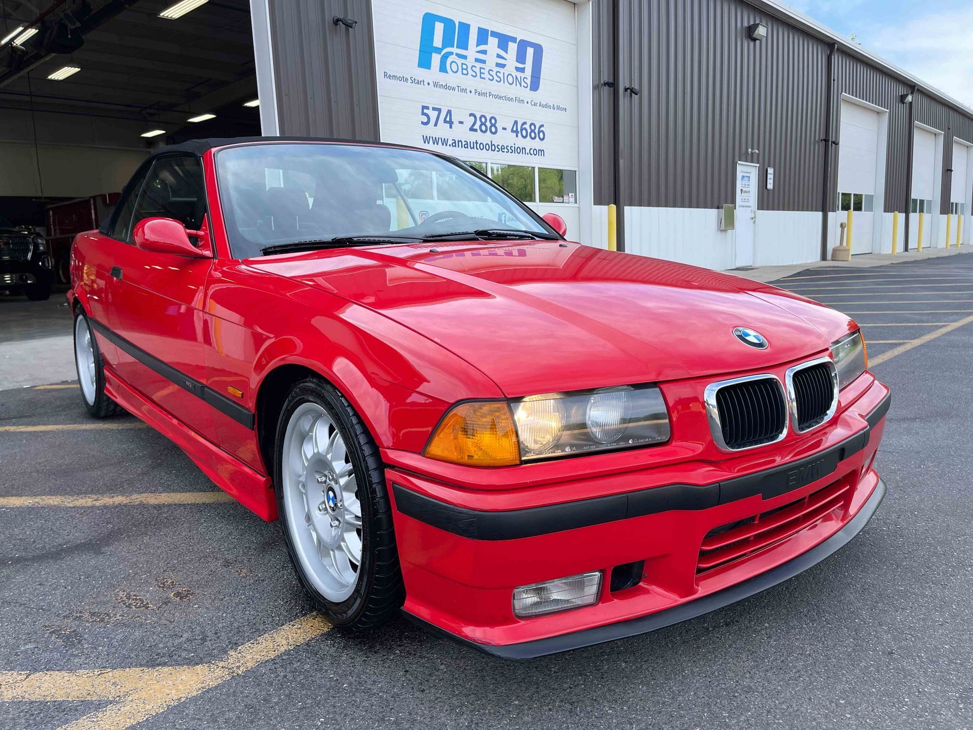 Red BMW convertible parked in front of an auto shop.