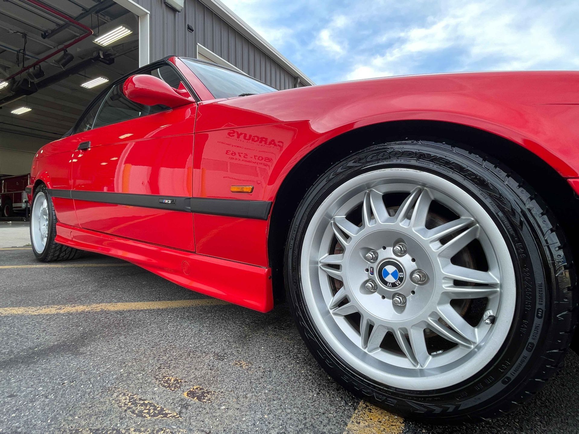 Red BMW convertible with silver wheels parked on pavement.