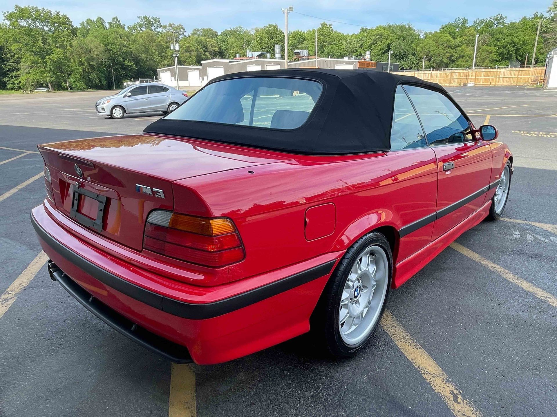 Red BMW M3 convertible with a black soft top in a parking lot.