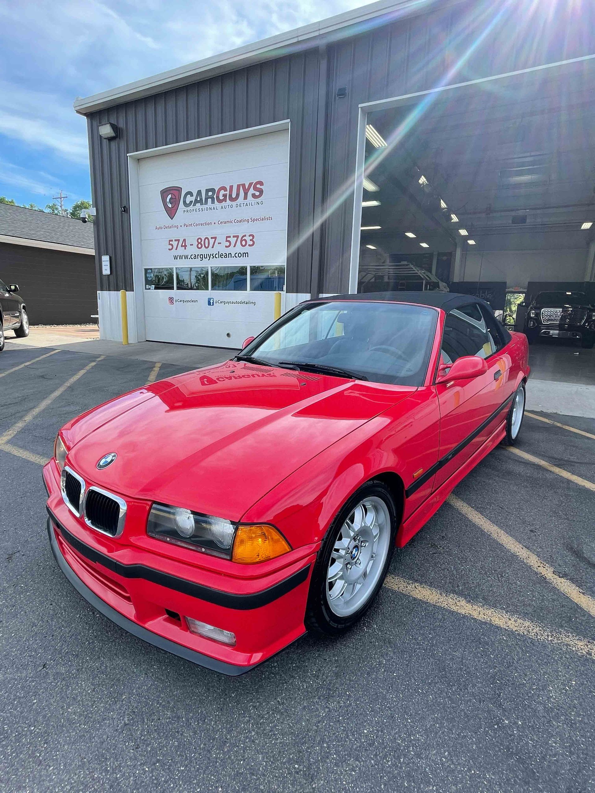Red BMW convertible parked in front of an auto repair shop with open garage doors.