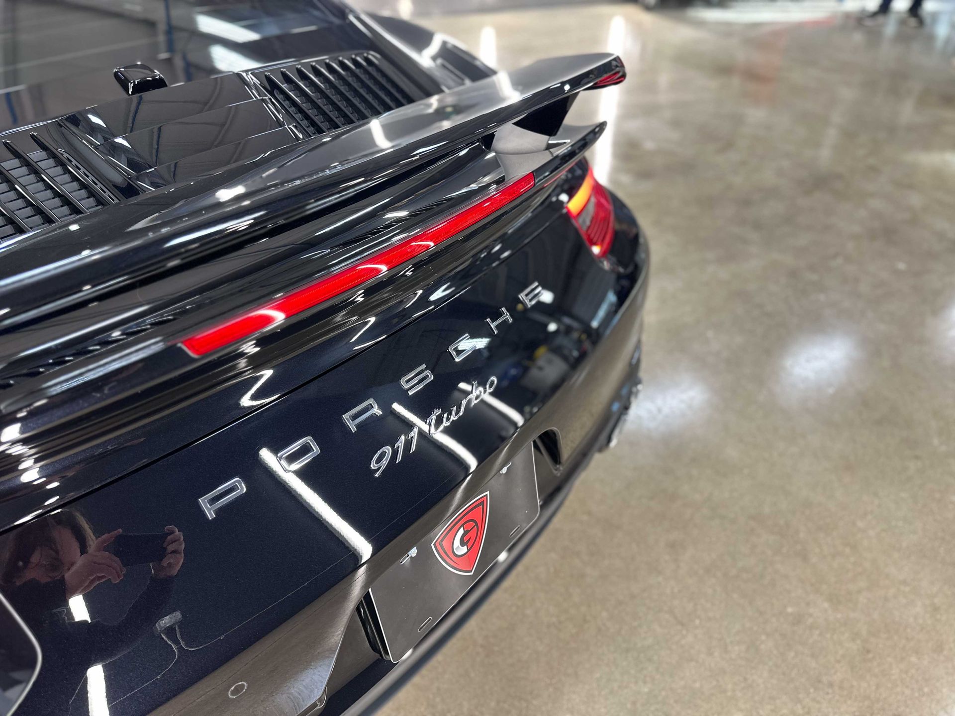 Black Porsche 911 Turbo with red taillight and badging, parked on concrete.
