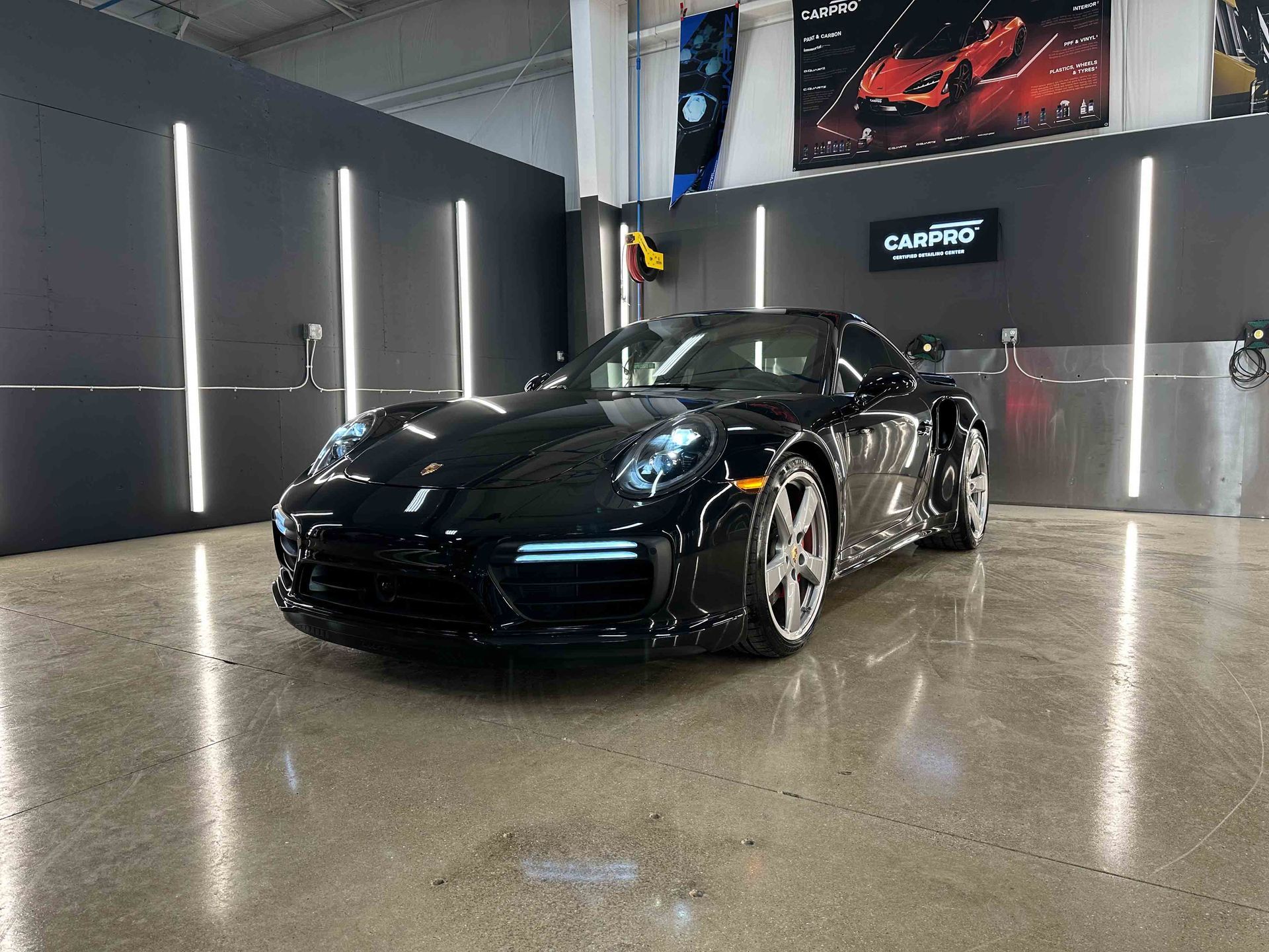 Black Porsche sports car in a modern garage with bright lights.