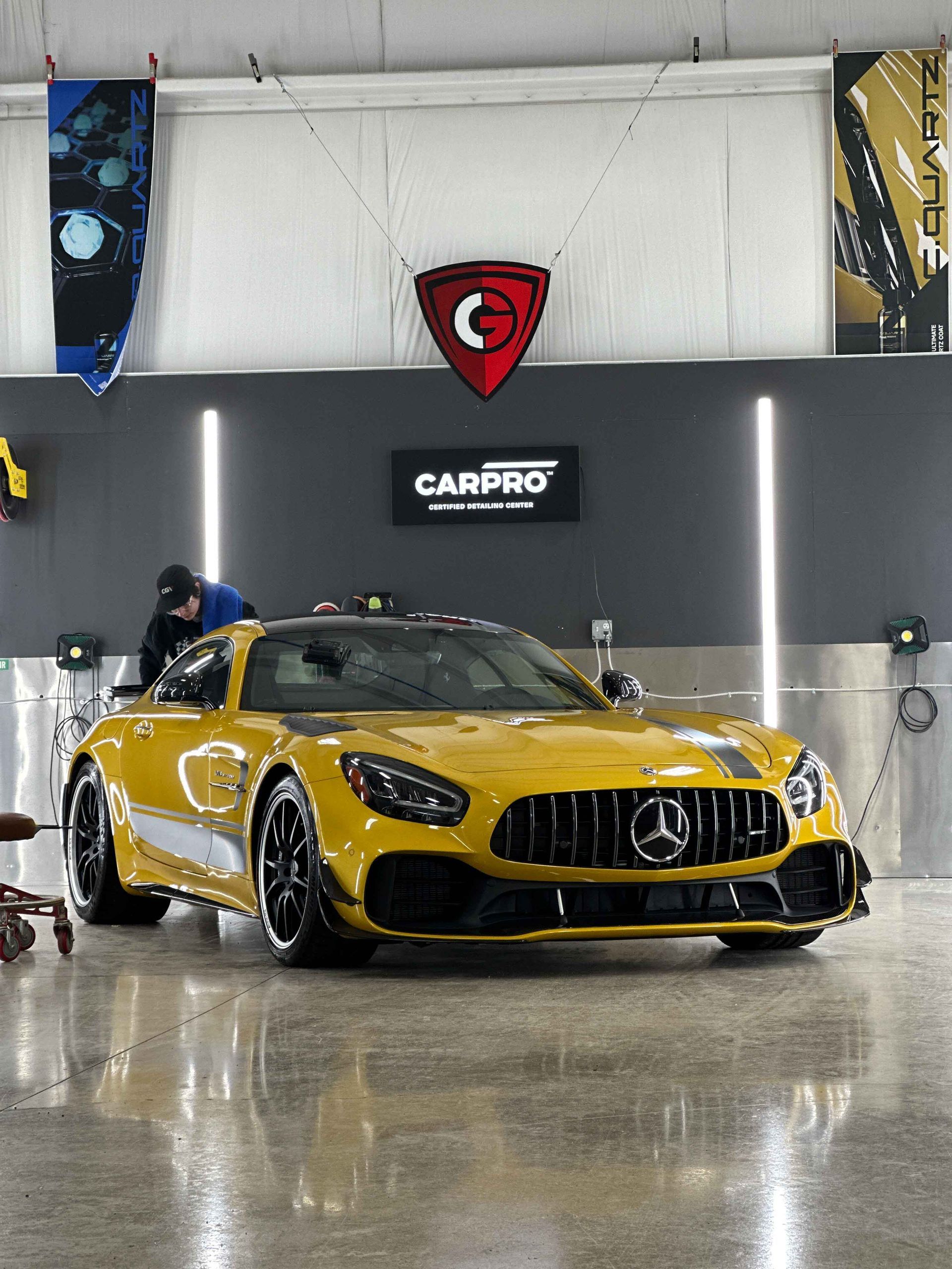 Yellow Mercedes-AMG GT being detailed inside a garage. A person works on the car.