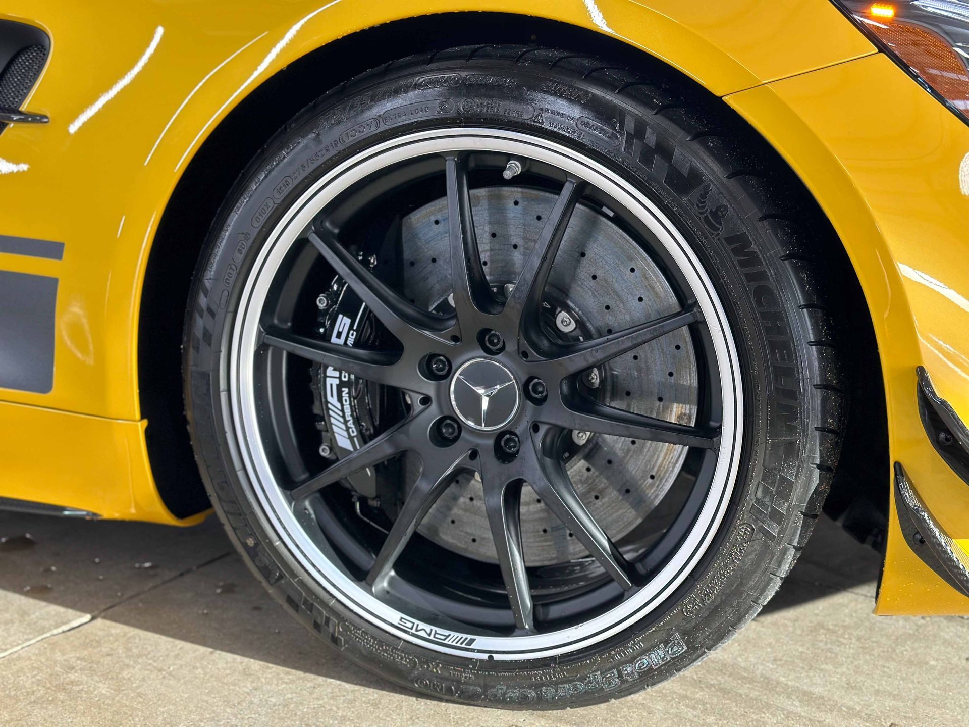 Close-up of a yellow sports car's black wheel with a silver rim and the Mercedes-Benz logo.