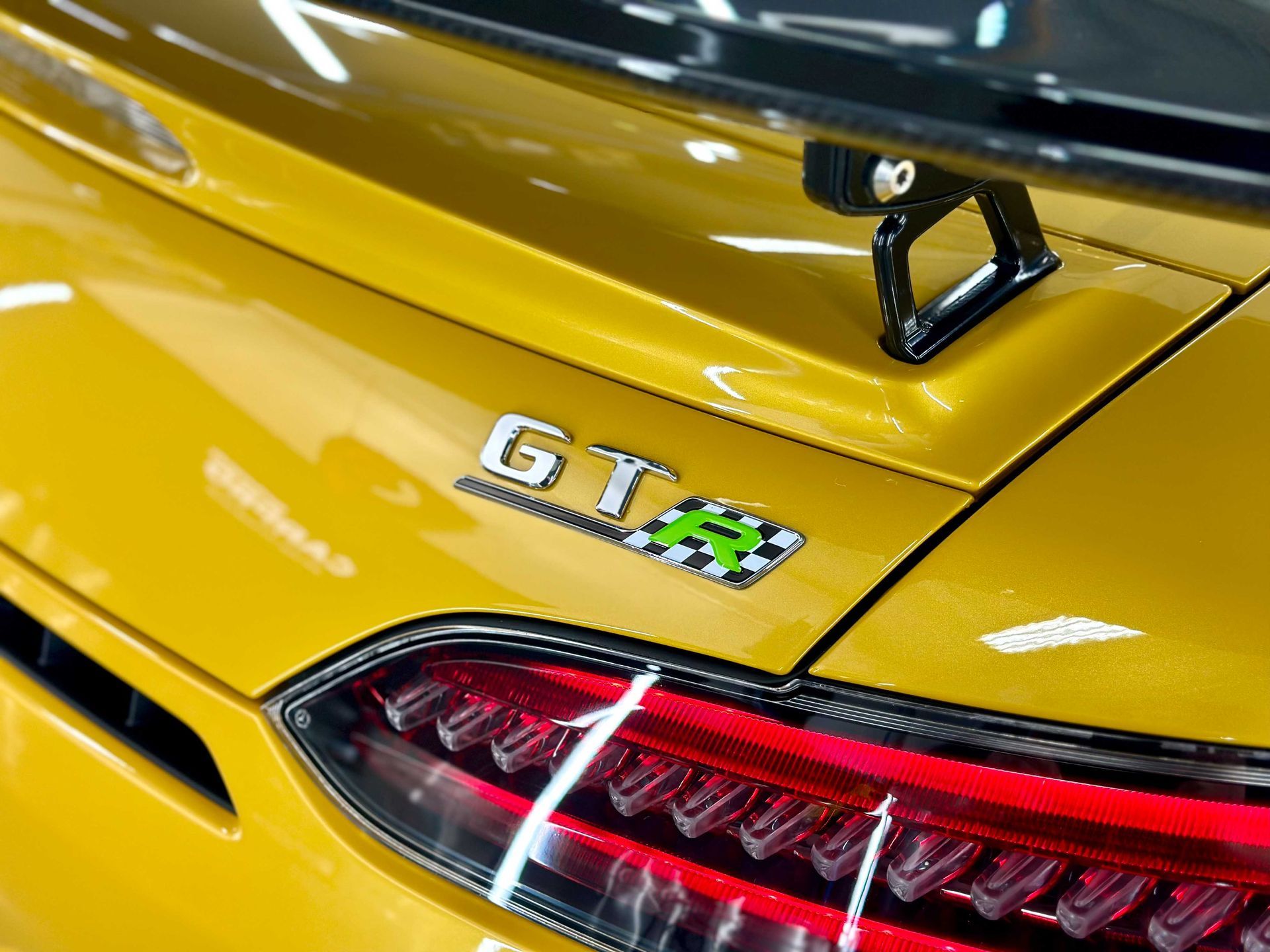 Close-up of a yellow Mercedes-AMG GT's rear, showing the GT badge and a black spoiler.