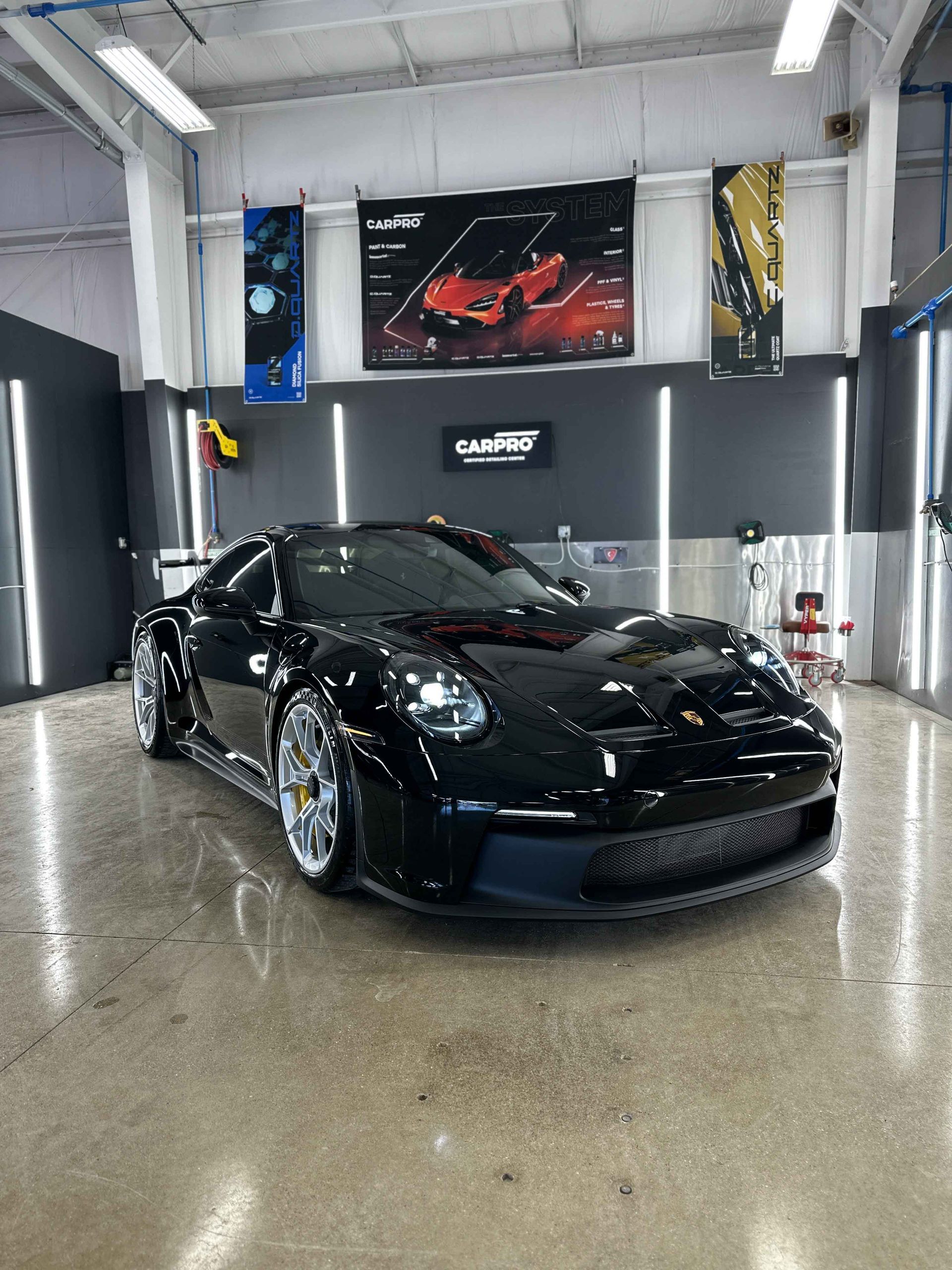 Black Porsche 911 GT3 in a car detailing bay, with gray walls and bright lighting.