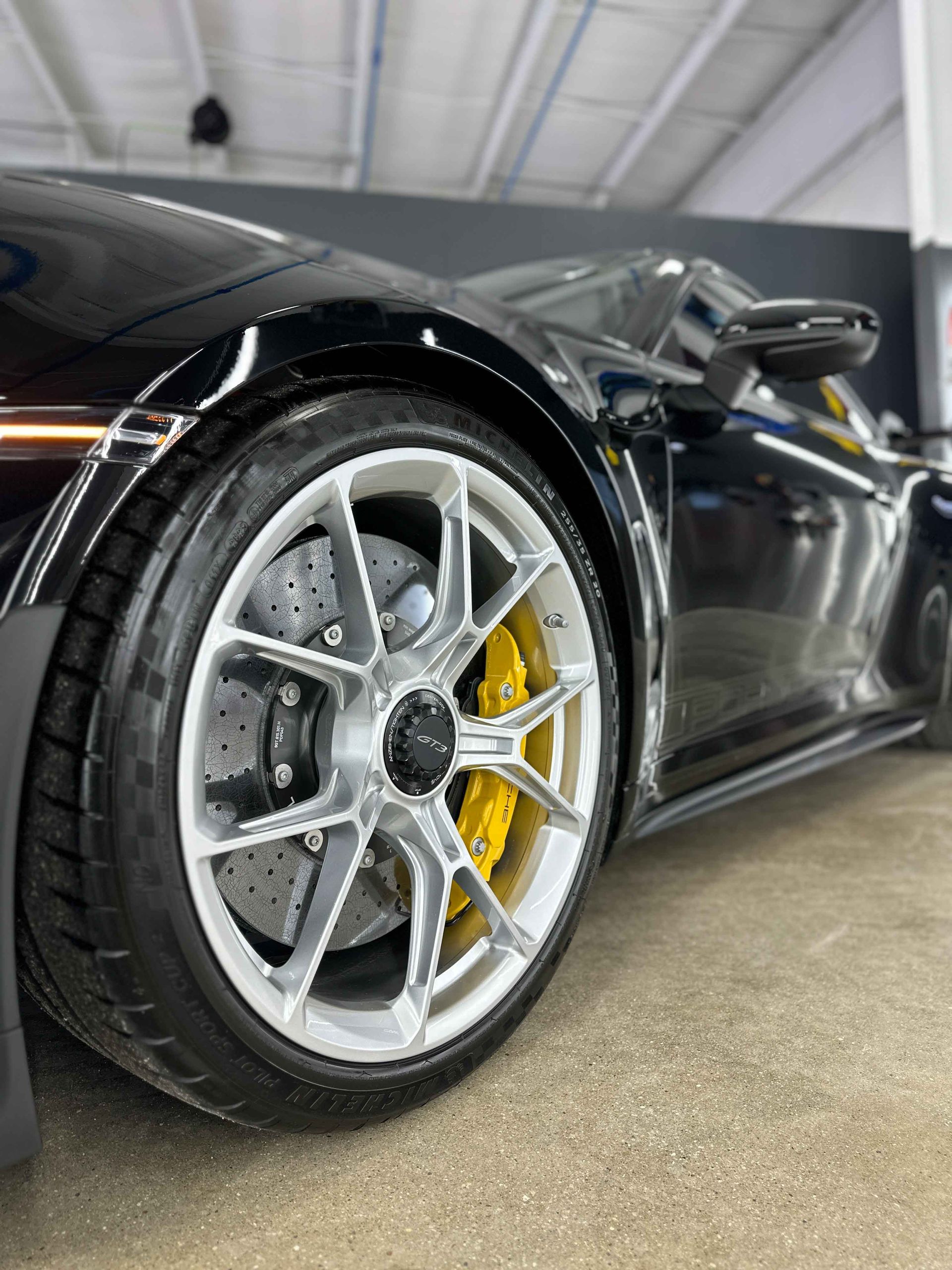 A person wearing black gloves is polishing a black car