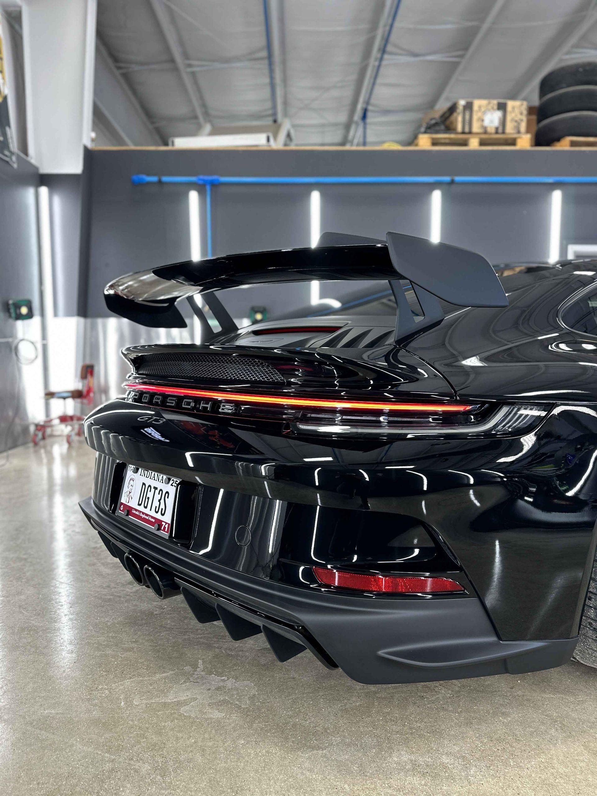 Black Porsche sports car in a garage, showcasing rear wing, lights, and bumper.