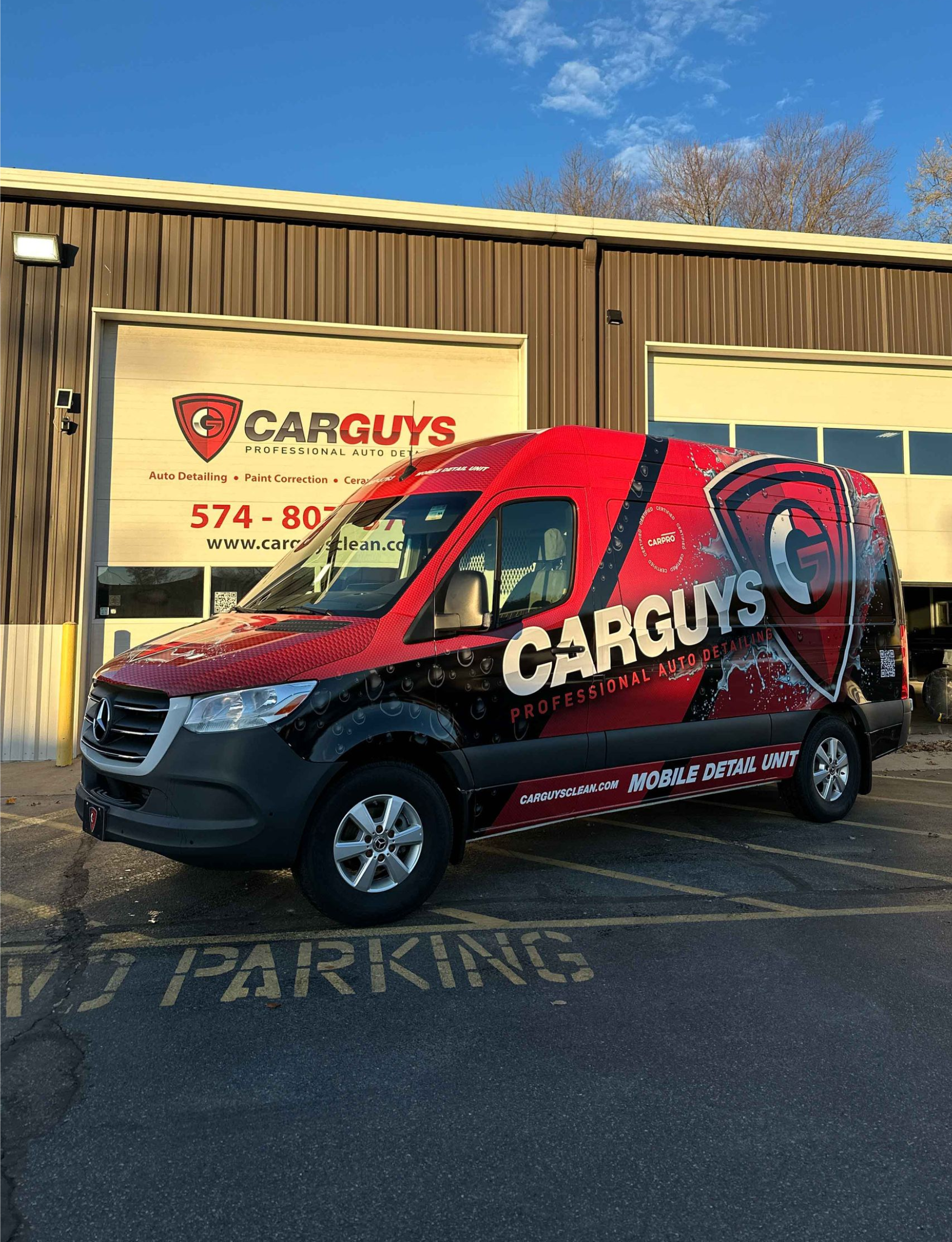 Two men applying protective film to the hood of a white truck in a shop.