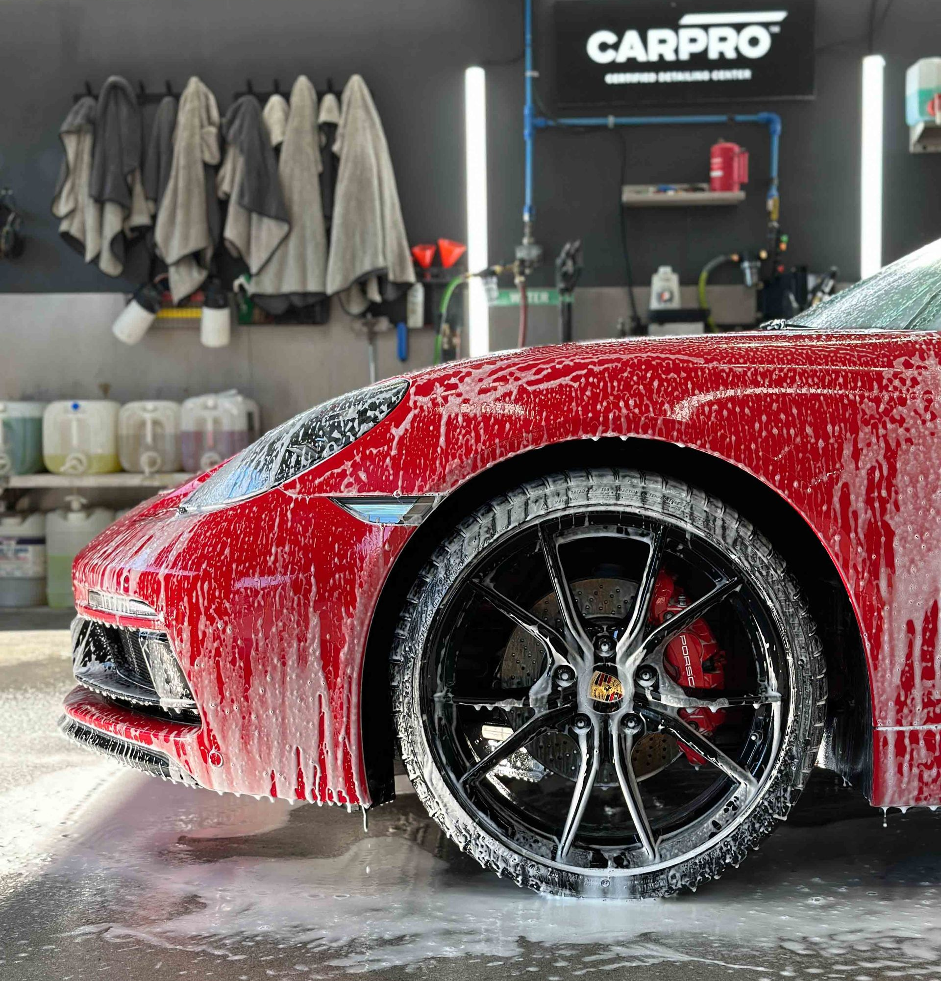A person wearing black gloves is polishing the hood of a red car.