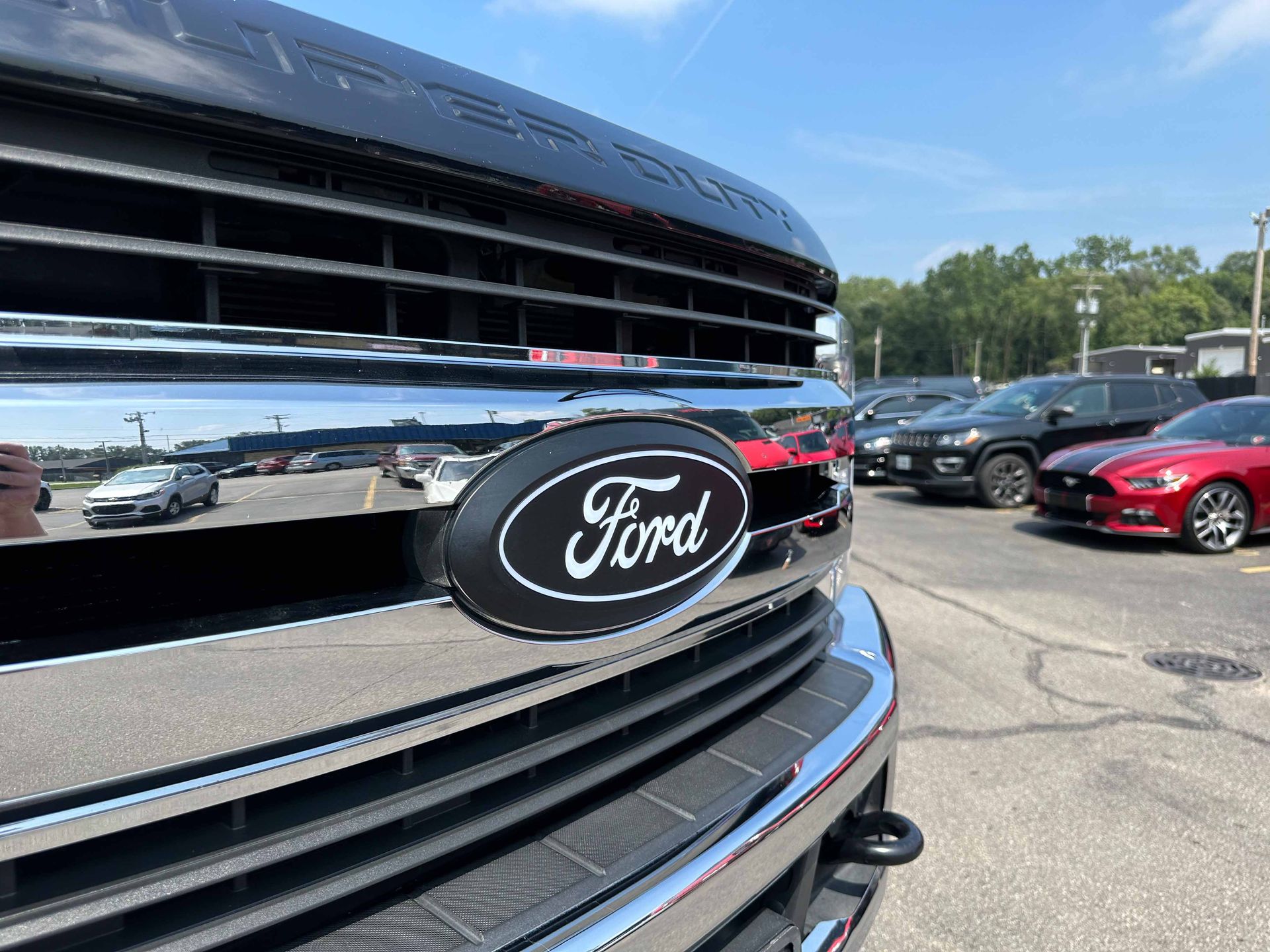 Black Ford Super Duty truck grill with Ford logo in front of other vehicles.