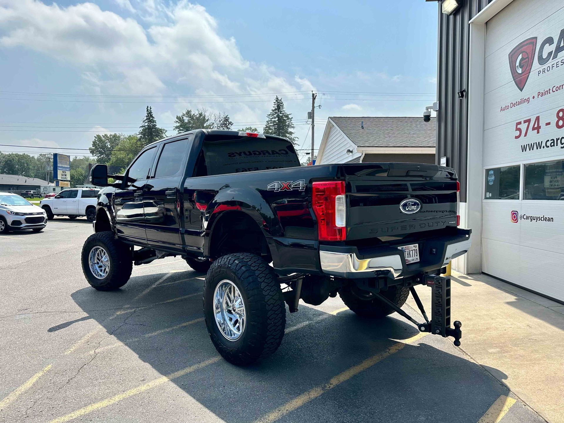 Black lifted Ford truck parked in front of a building with a business sign.