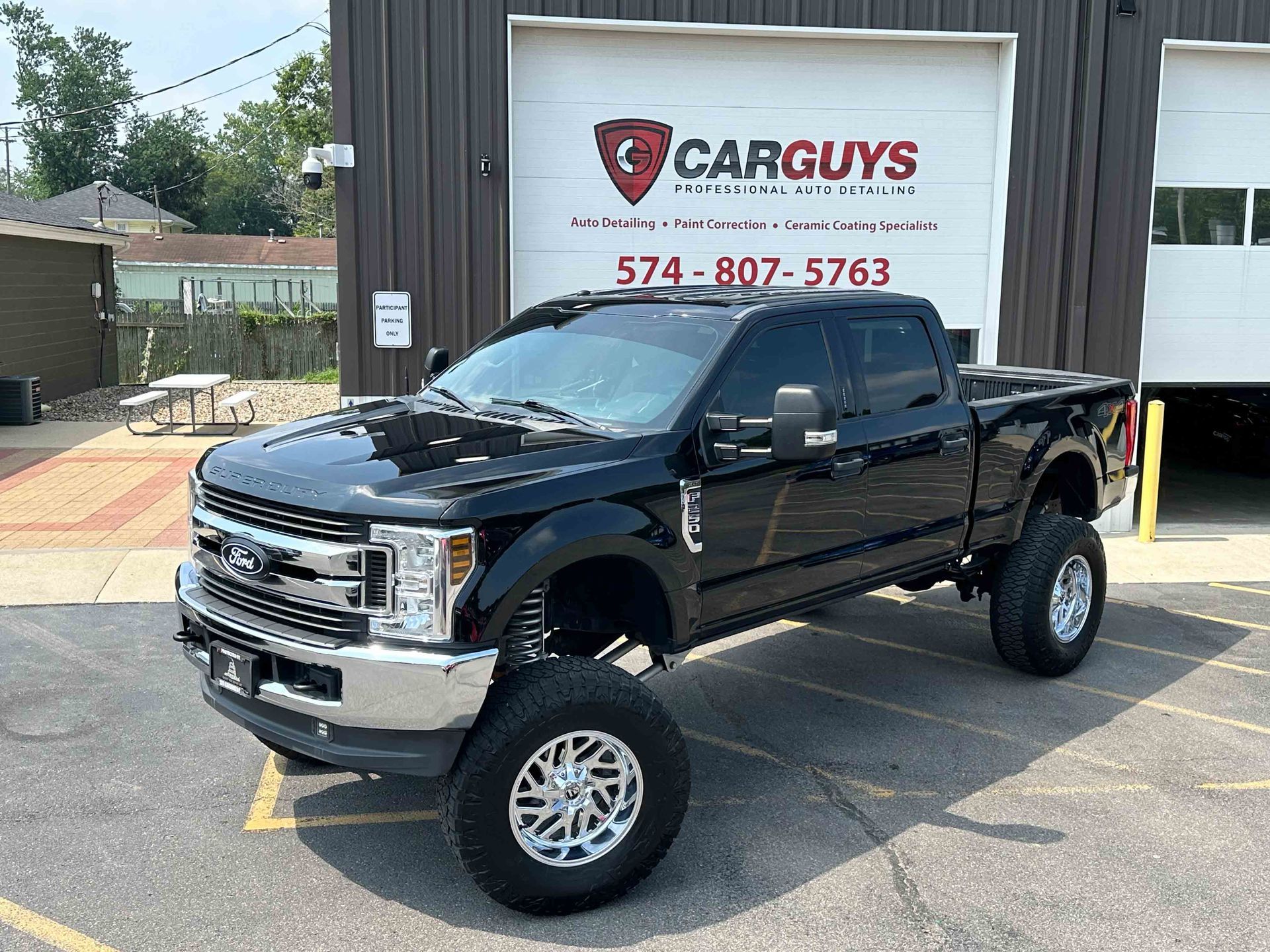 Black lifted Ford truck parked in front of a car dealership.
