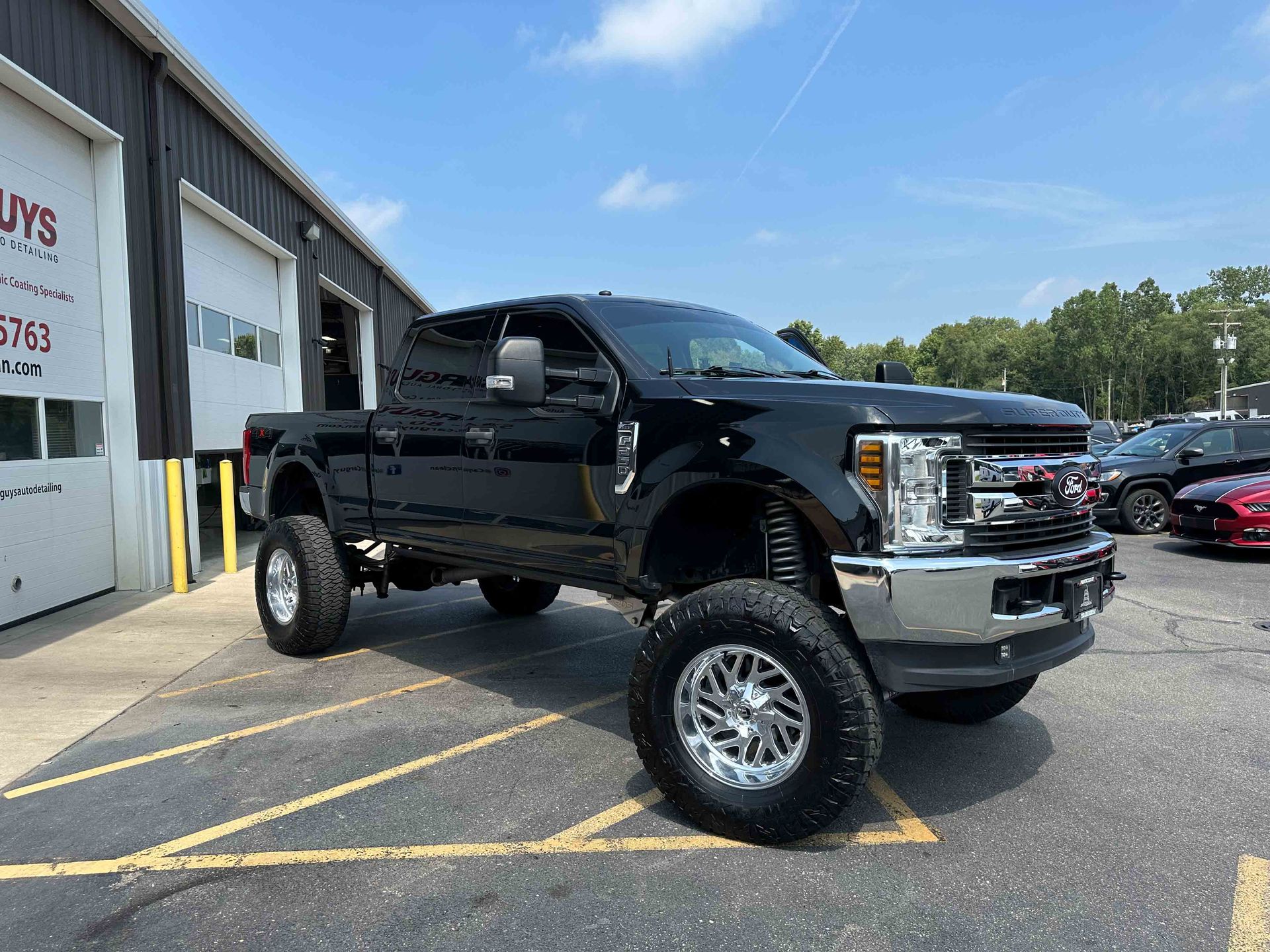 Black lifted Ford pickup truck parked outside a business under a blue sky.