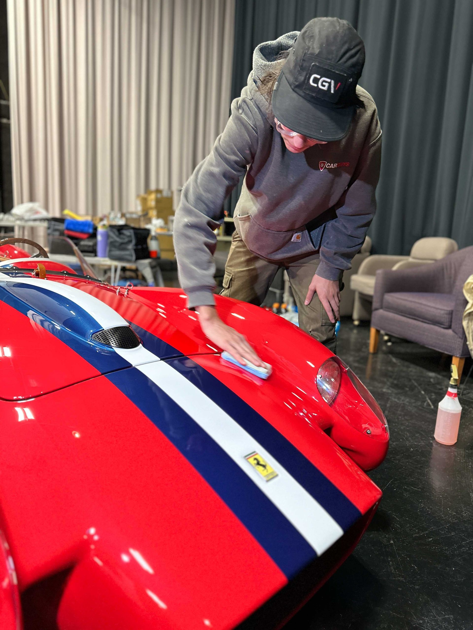 A person is polishing the hood of a blue car.