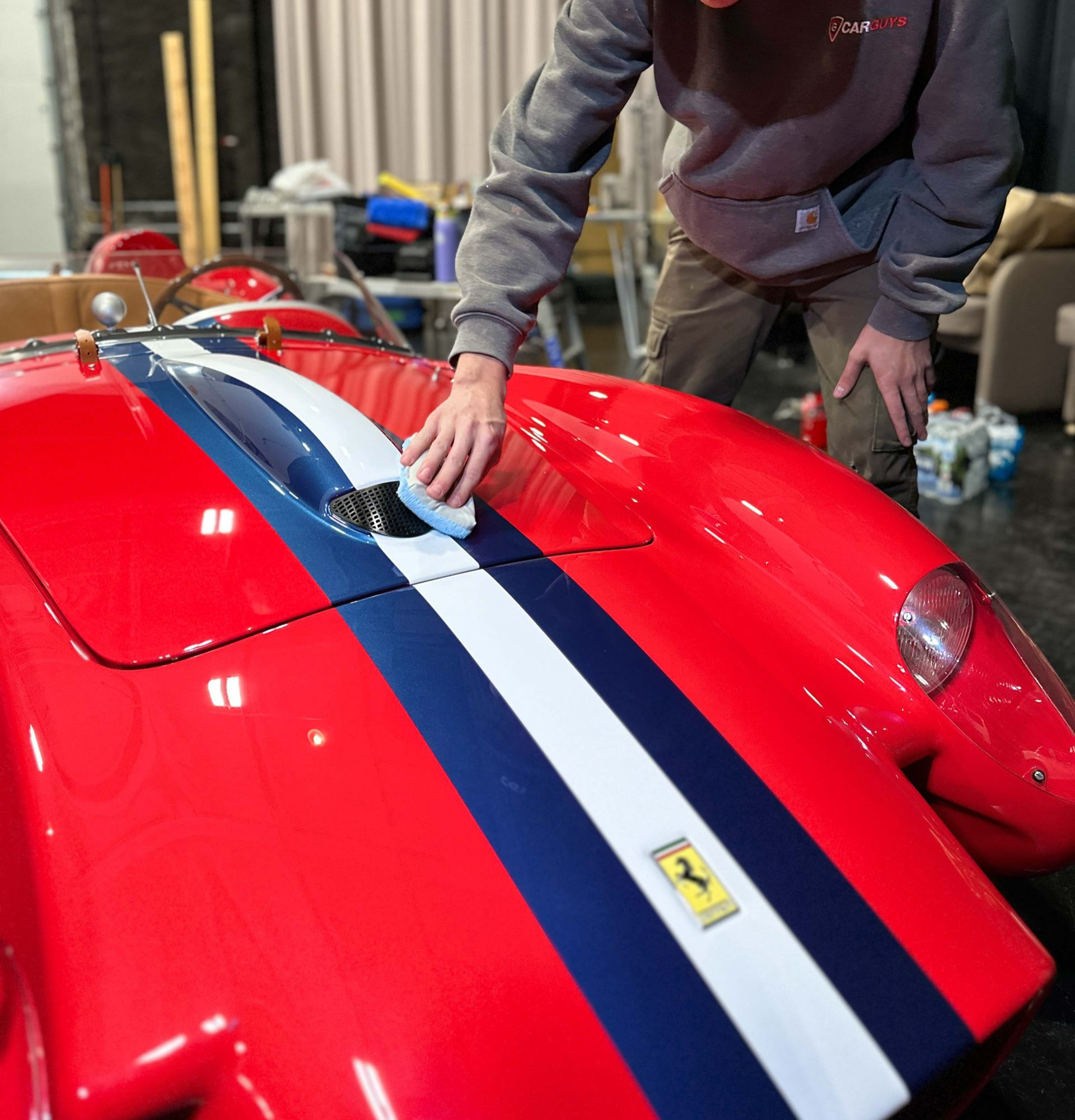 A person wearing black gloves is polishing the hood of a red car.