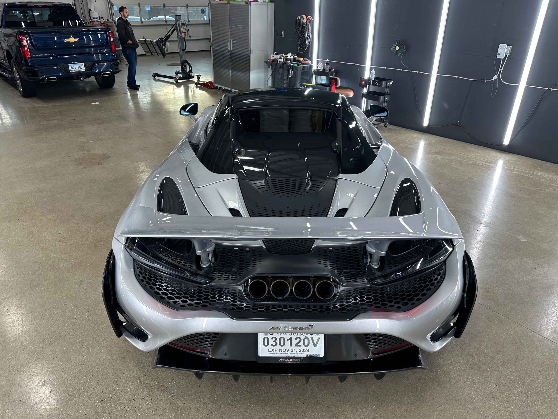 Silver McLaren sports car in a garage, black accents, license plate visible.