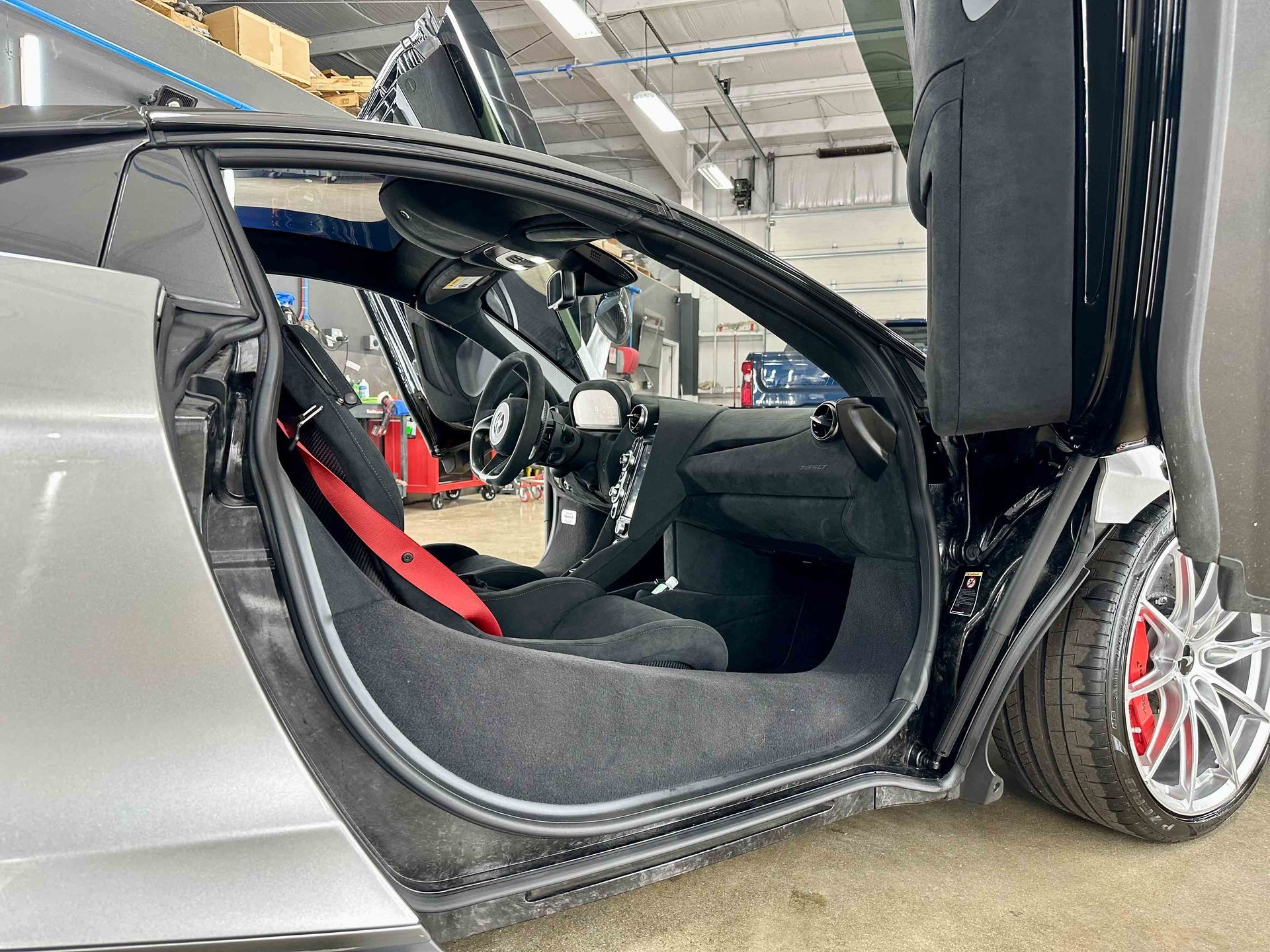 Silver sports car with open gullwing door, red seat belt, black interior.