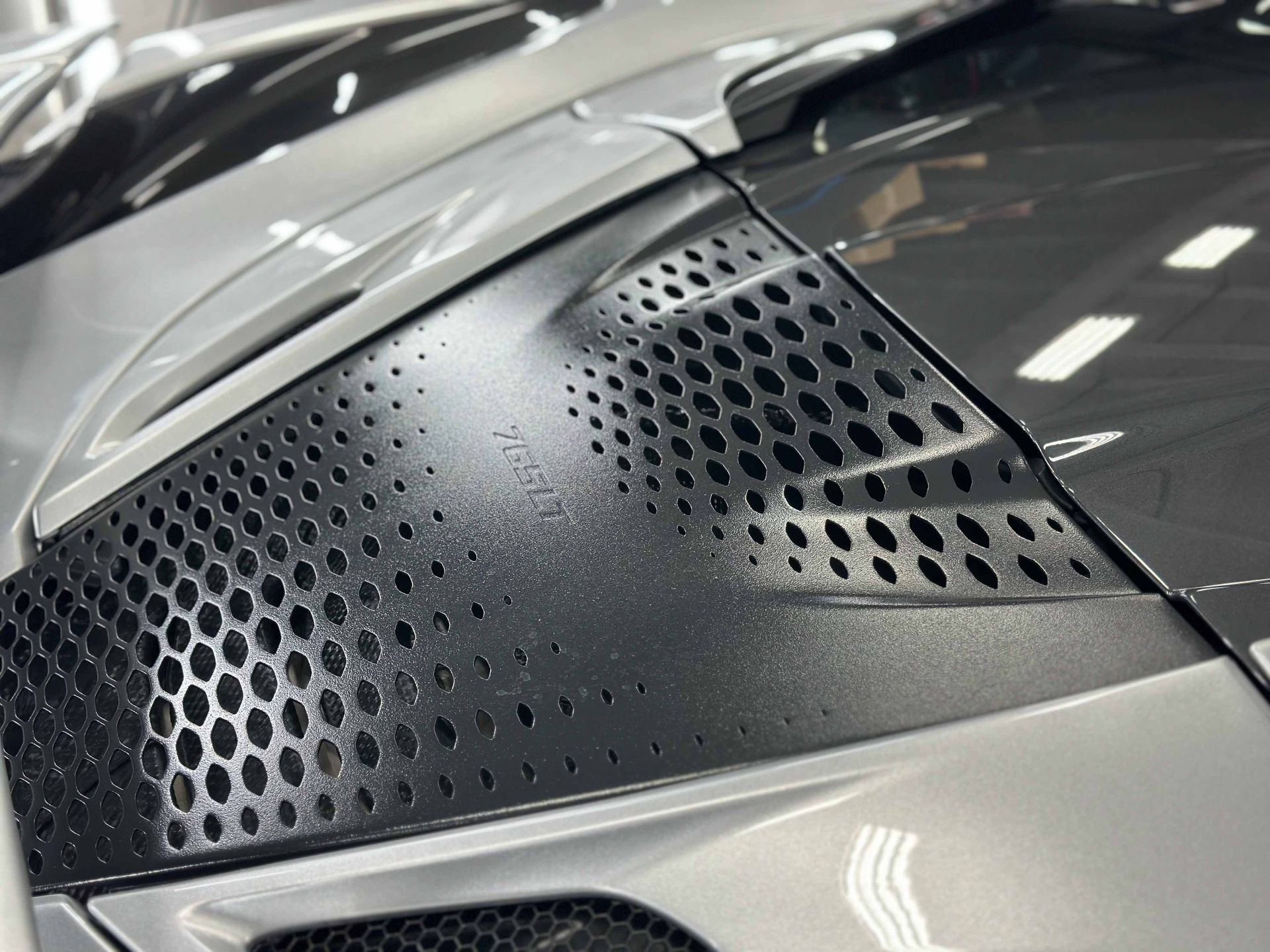 Gray car hood with a honeycomb-patterned vent.
