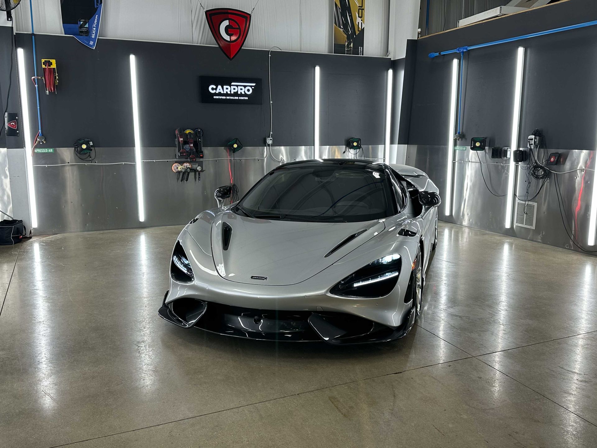 Silver McLaren sports car in a detailing shop, surrounded by lights and equipment.