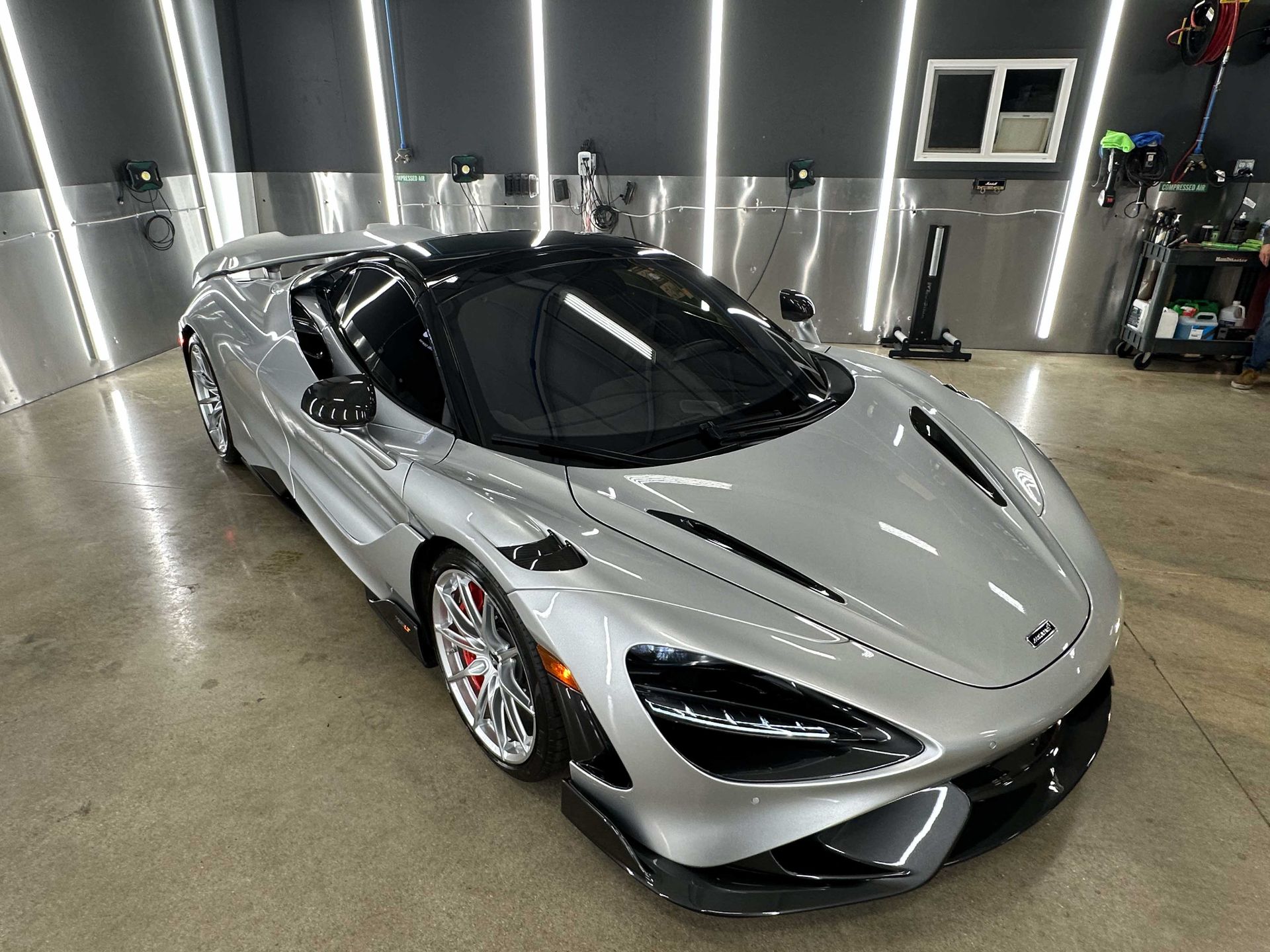 Silver McLaren sports car in a garage with bright lights.