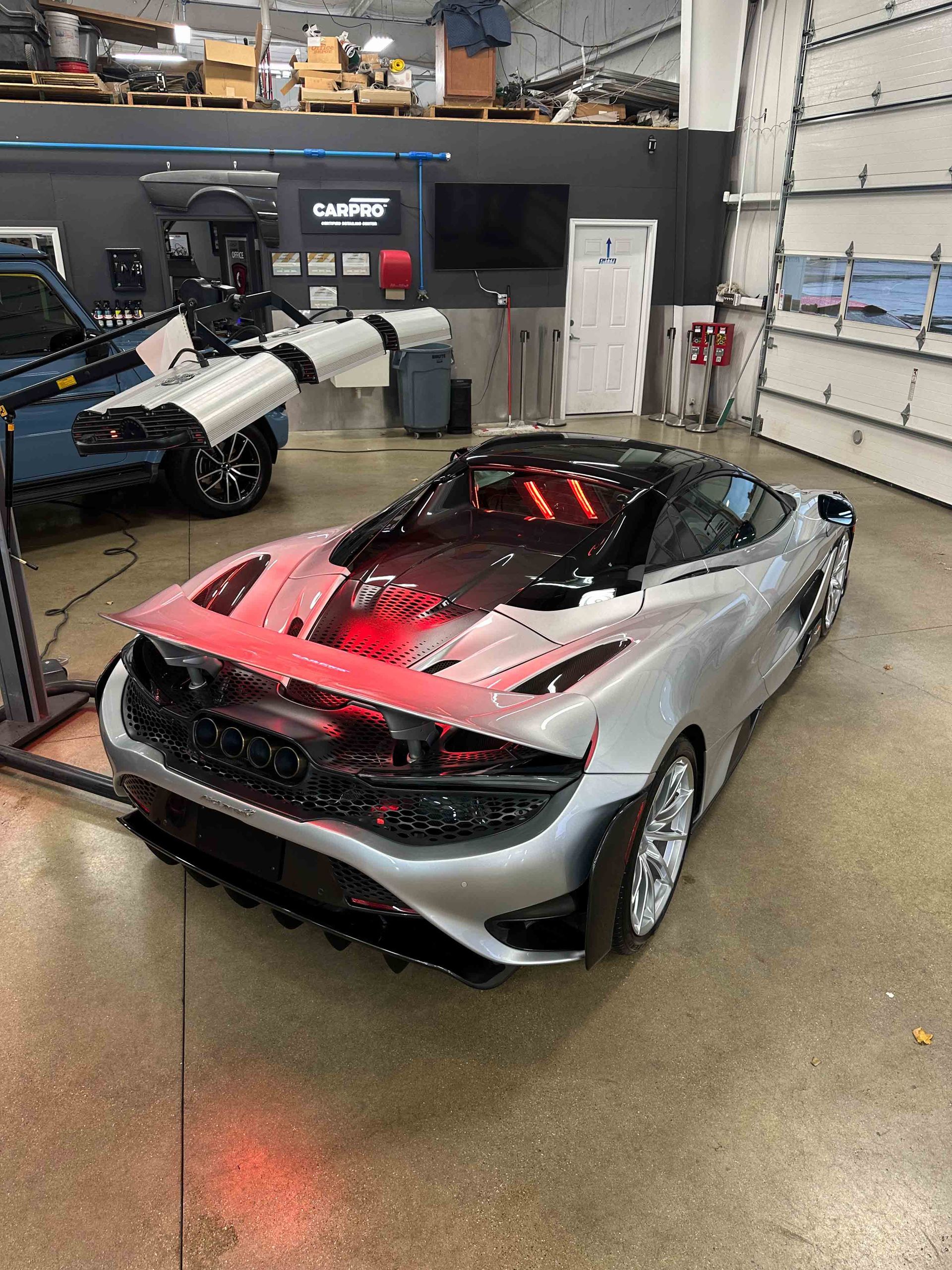 Silver McLaren sports car inside a garage, with red lights and a partially open door.