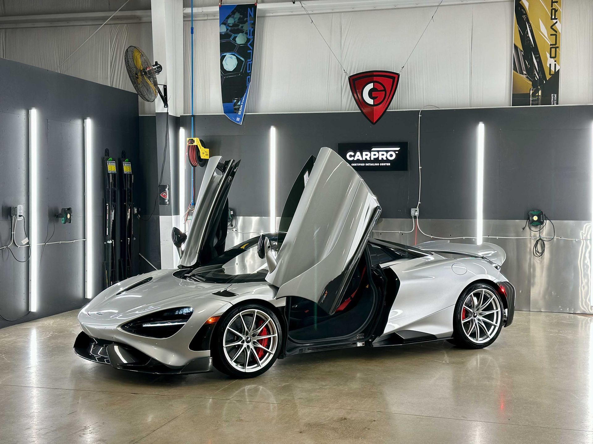 Silver McLaren supercar with doors open inside a detailing shop.