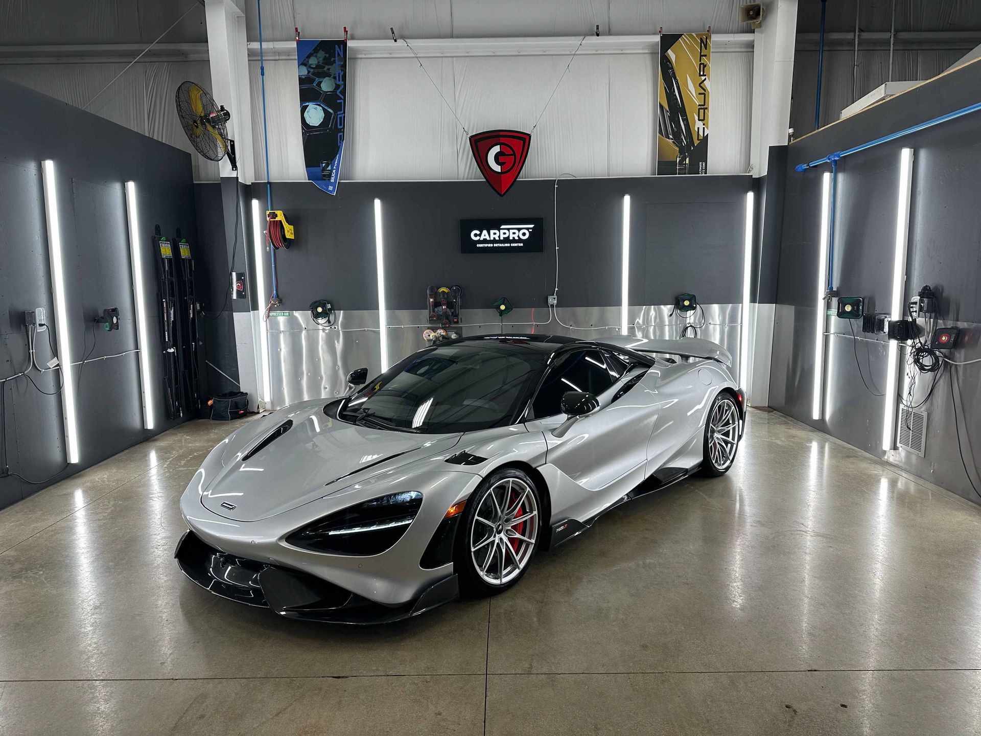 Silver McLaren sports car inside a detailing bay, under bright lights.
