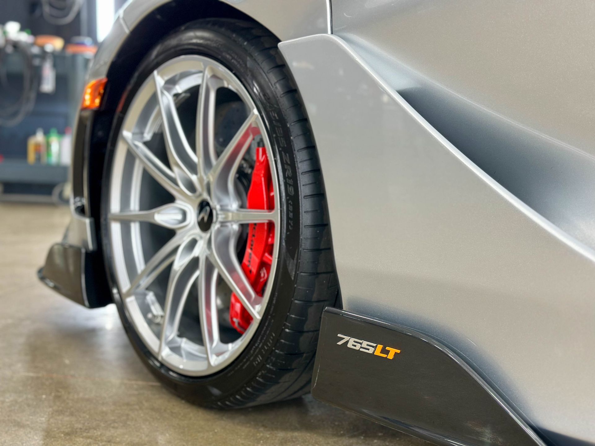 Silver McLaren 765LT sports car wheel, red brake caliper, carbon fiber trim.