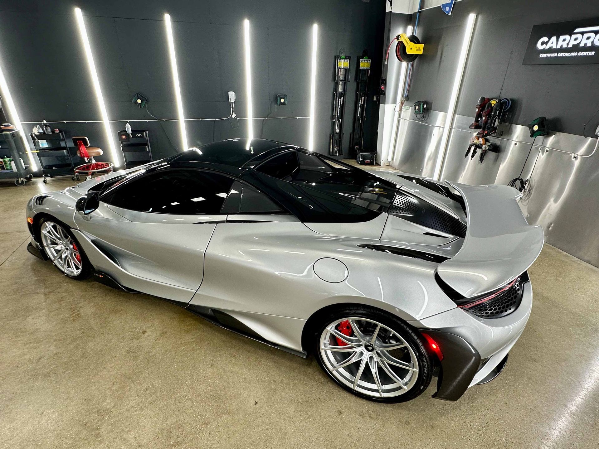 Silver McLaren sports car in a garage with black roof and spoiler; red brake calipers.
