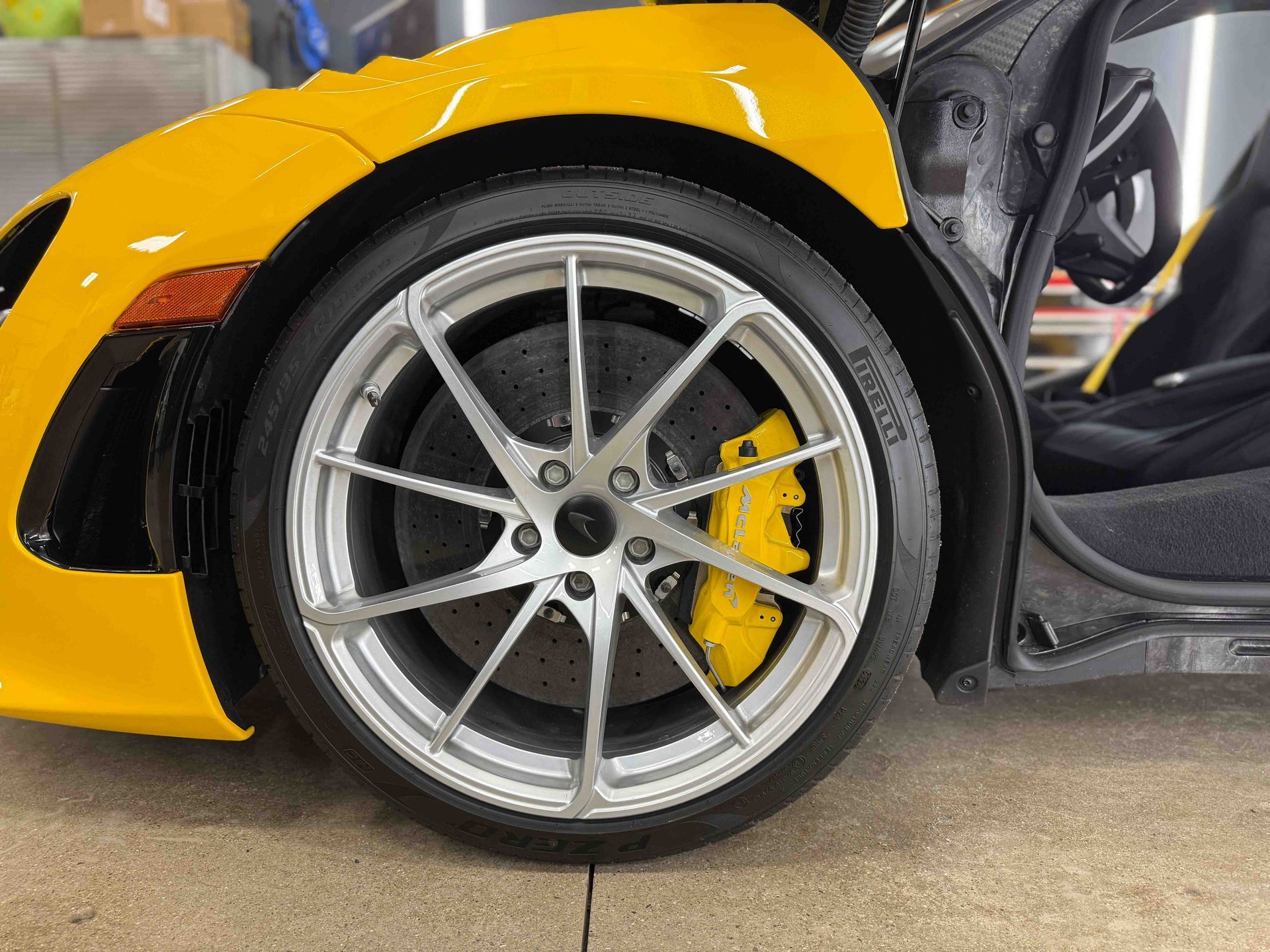 Yellow sports car with silver wheel, yellow brake caliper, black tire, and open door.