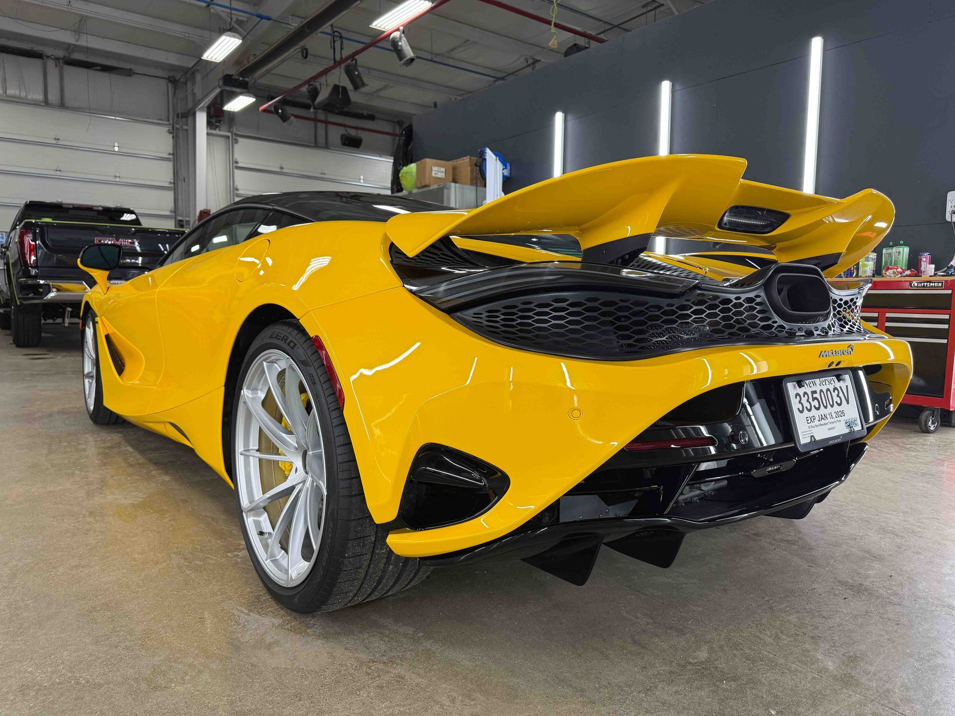 Yellow McLaren sports car, large spoiler, black accents, indoors, concrete floor.