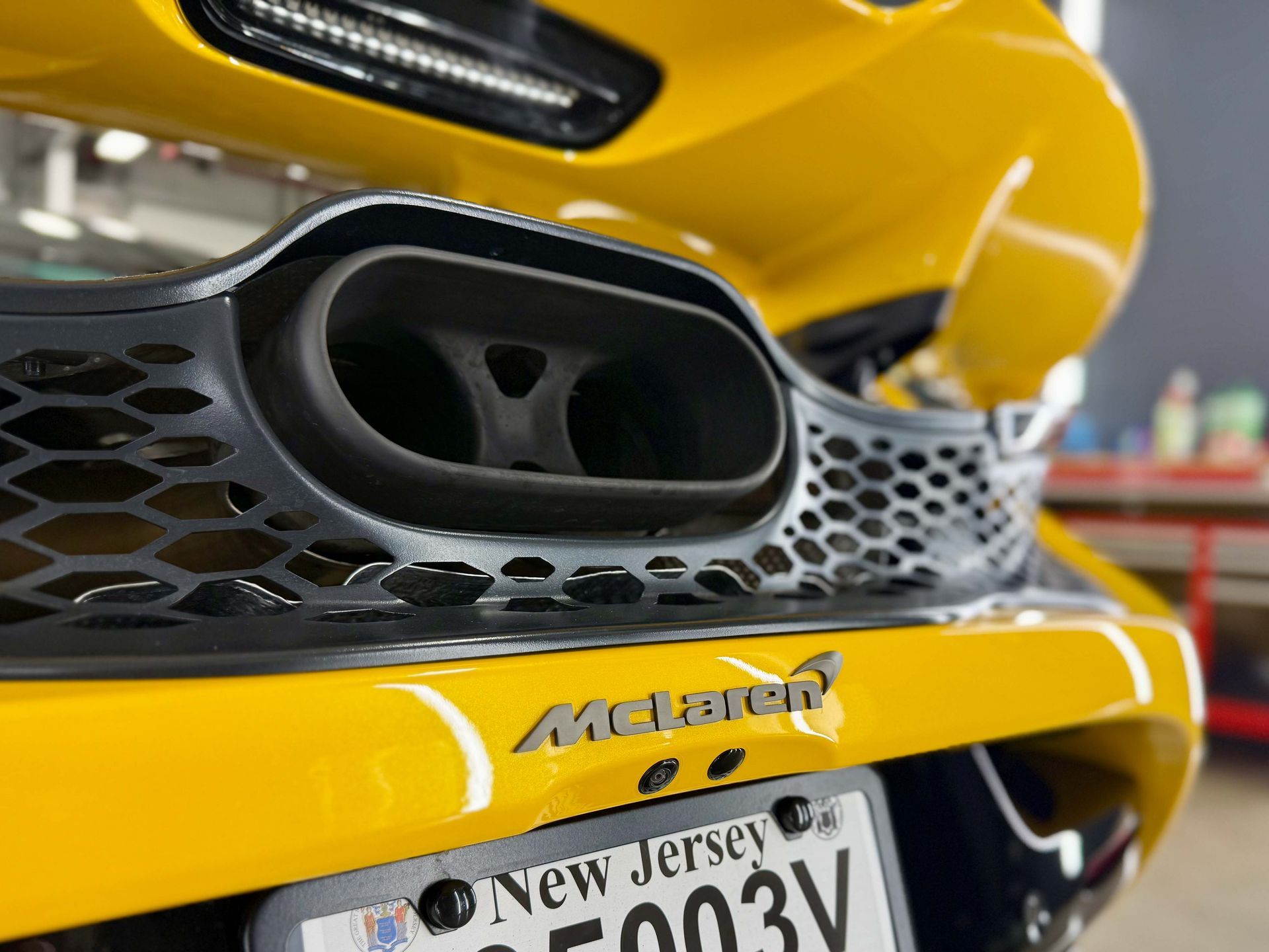 Close-up of a yellow McLaren's rear, featuring exhaust, honeycomb grill, and the 