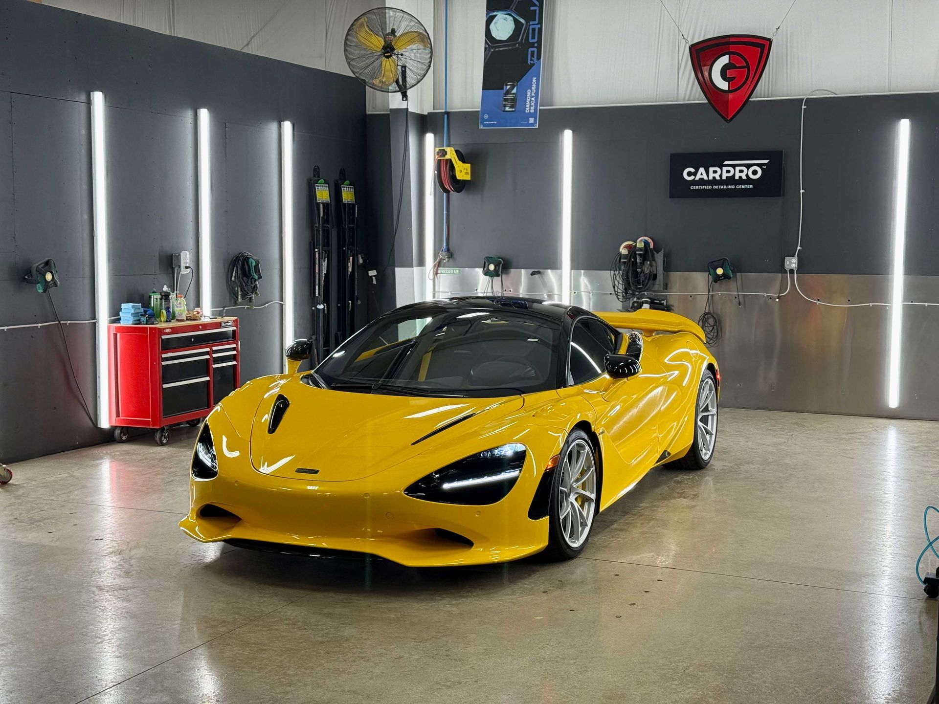 Yellow McLaren sports car in a detailing shop, under bright lights.
