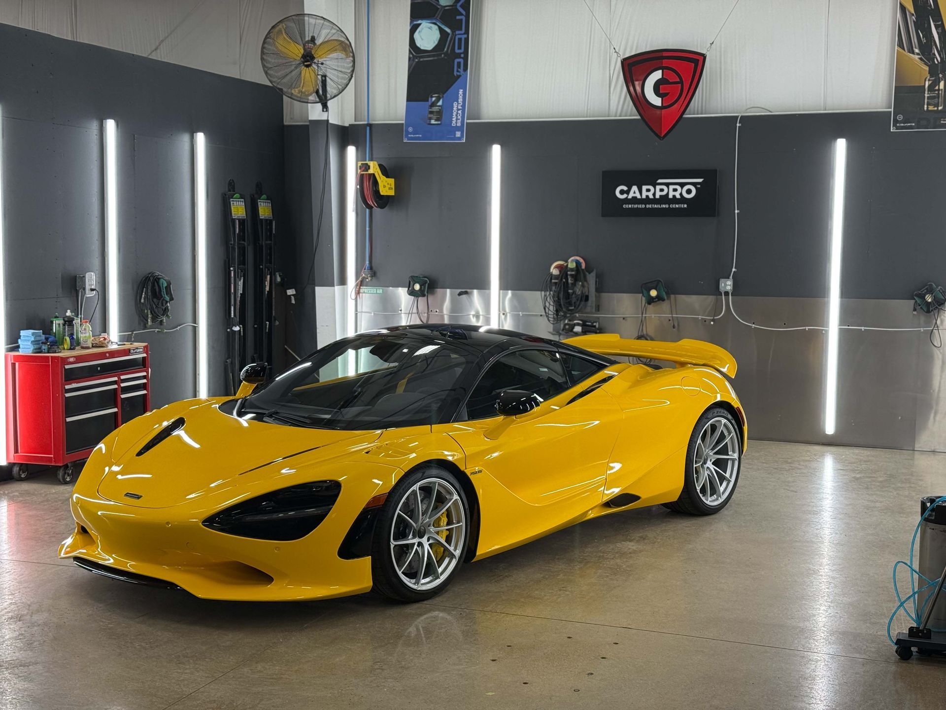 Yellow McLaren sports car in a garage with detailing equipment, under bright lights.
