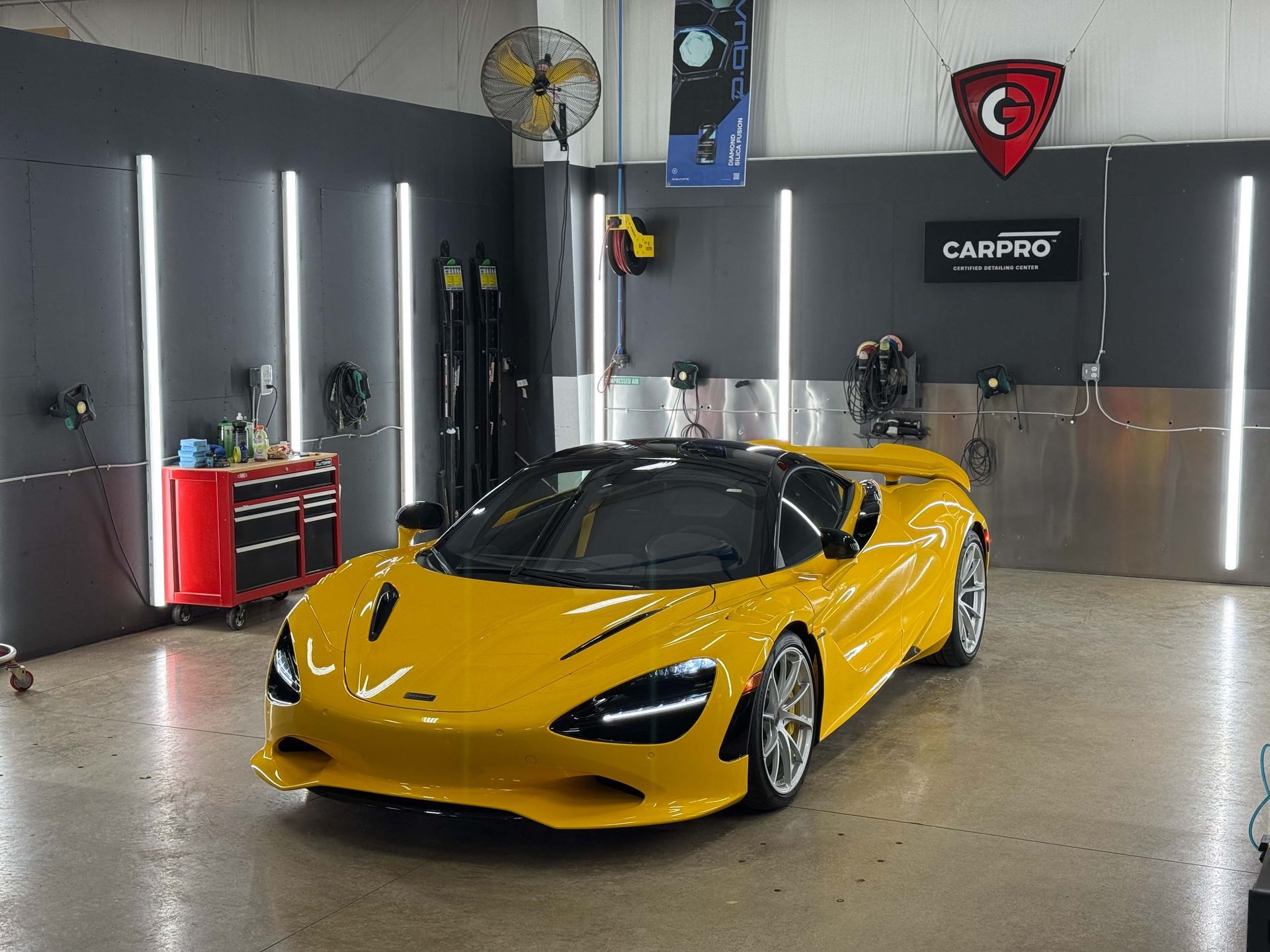 Yellow McLaren sports car in a garage with detailing equipment and vertical lights.